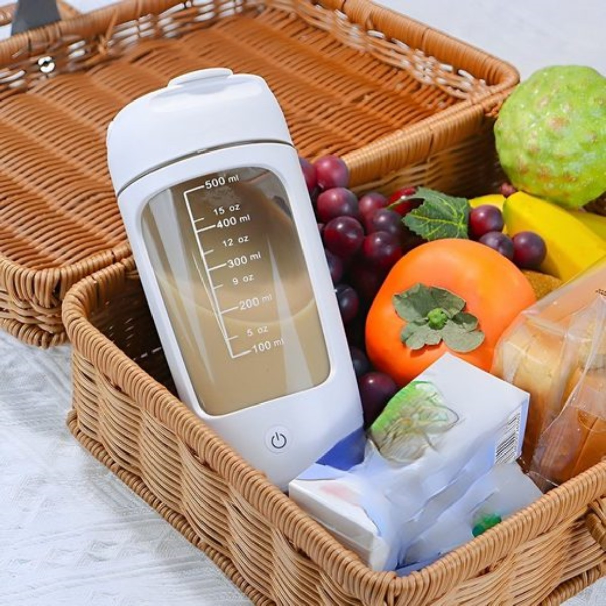 Weißer Mixer in einem Weidenkorb mit Obst: Trauben, Kaki, Banane und Saftpackung.