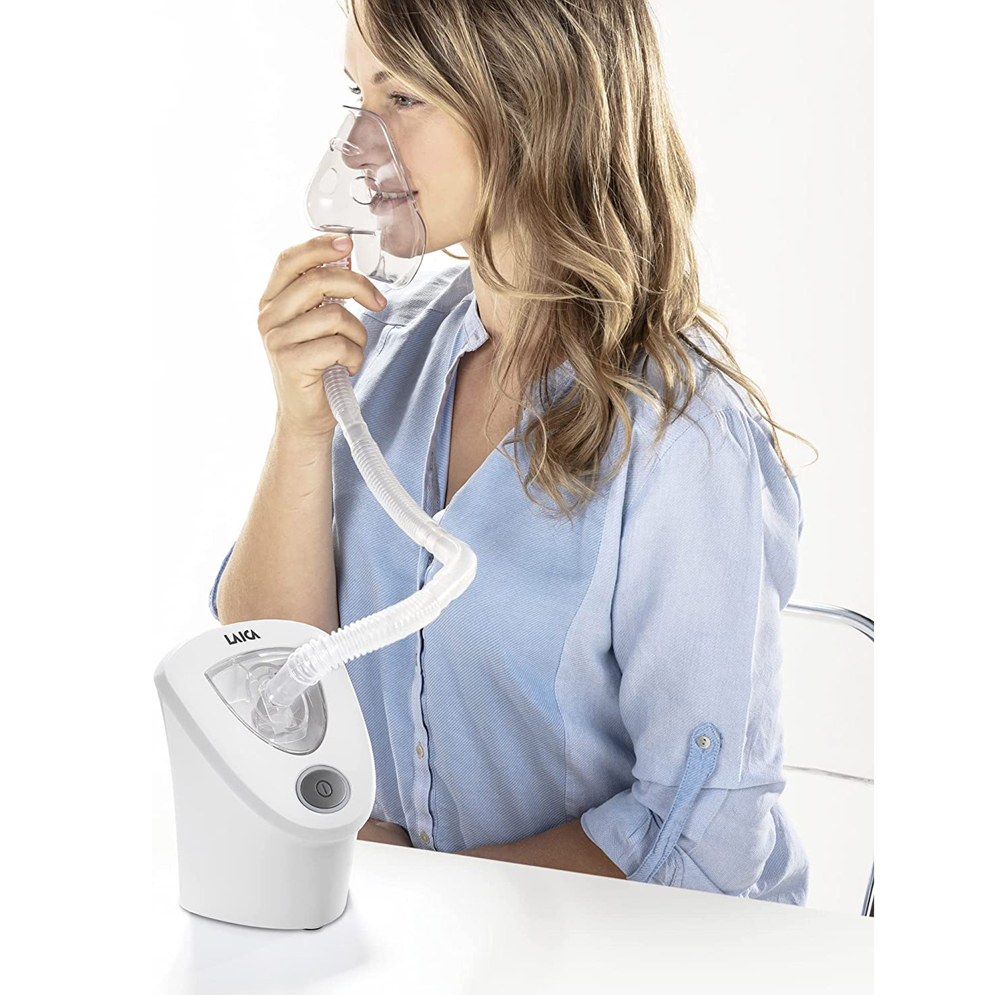 Mujer usando un nebulizador blanco con mascarilla, sentada en una mesa.