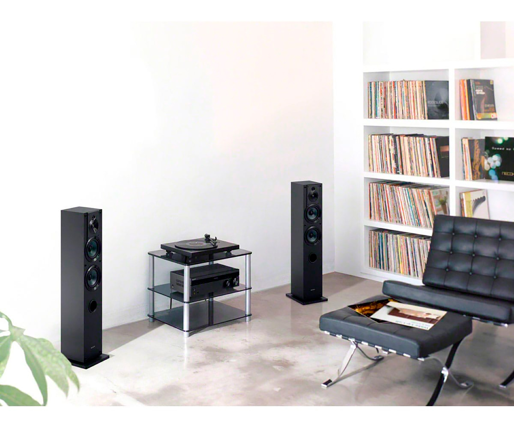Salón con altavoces, tocadiscos en soporte de cristal y sillón de cuero negro.