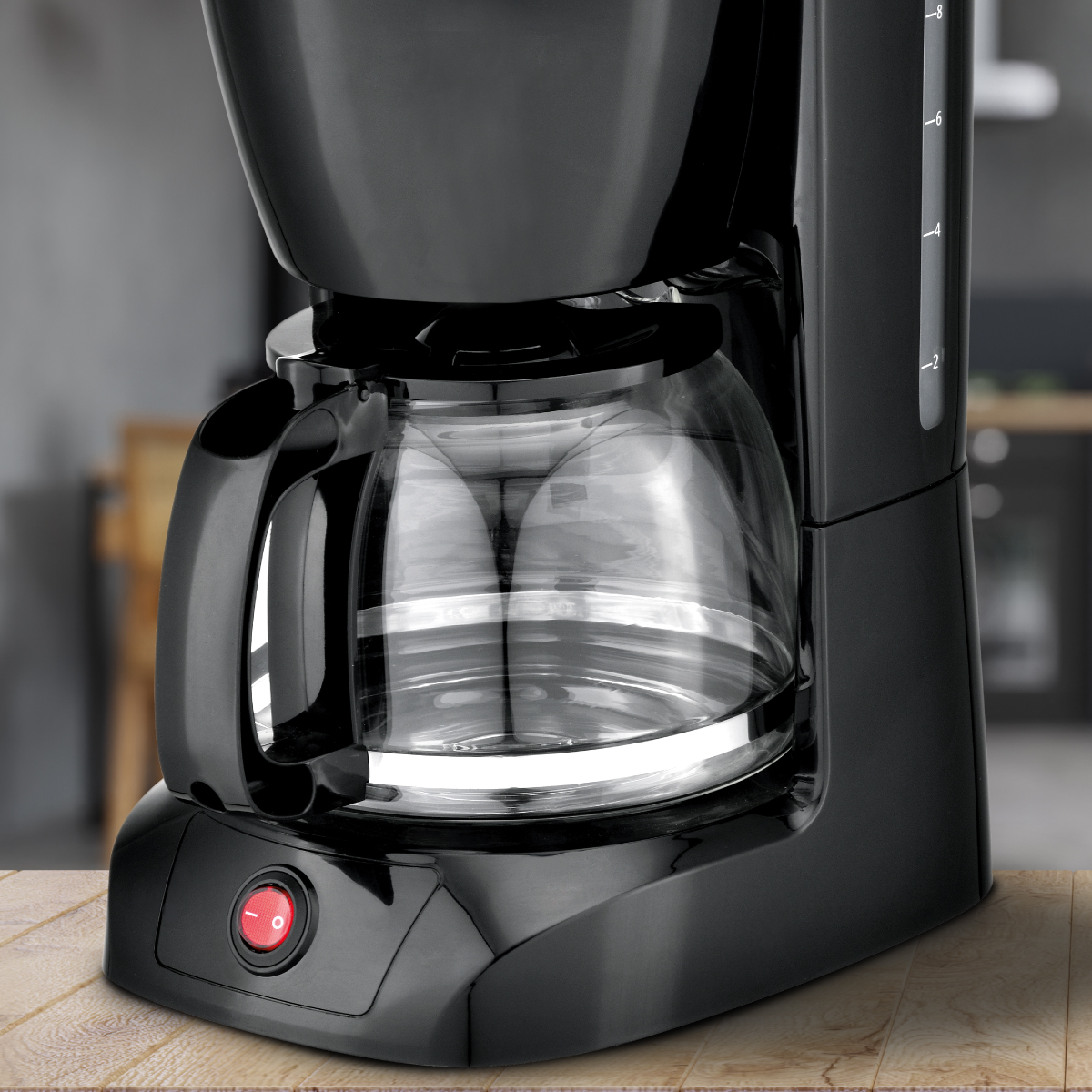 Cafetera negra con jarra de cristal sobre una superficie de madera, fondo borroso.
