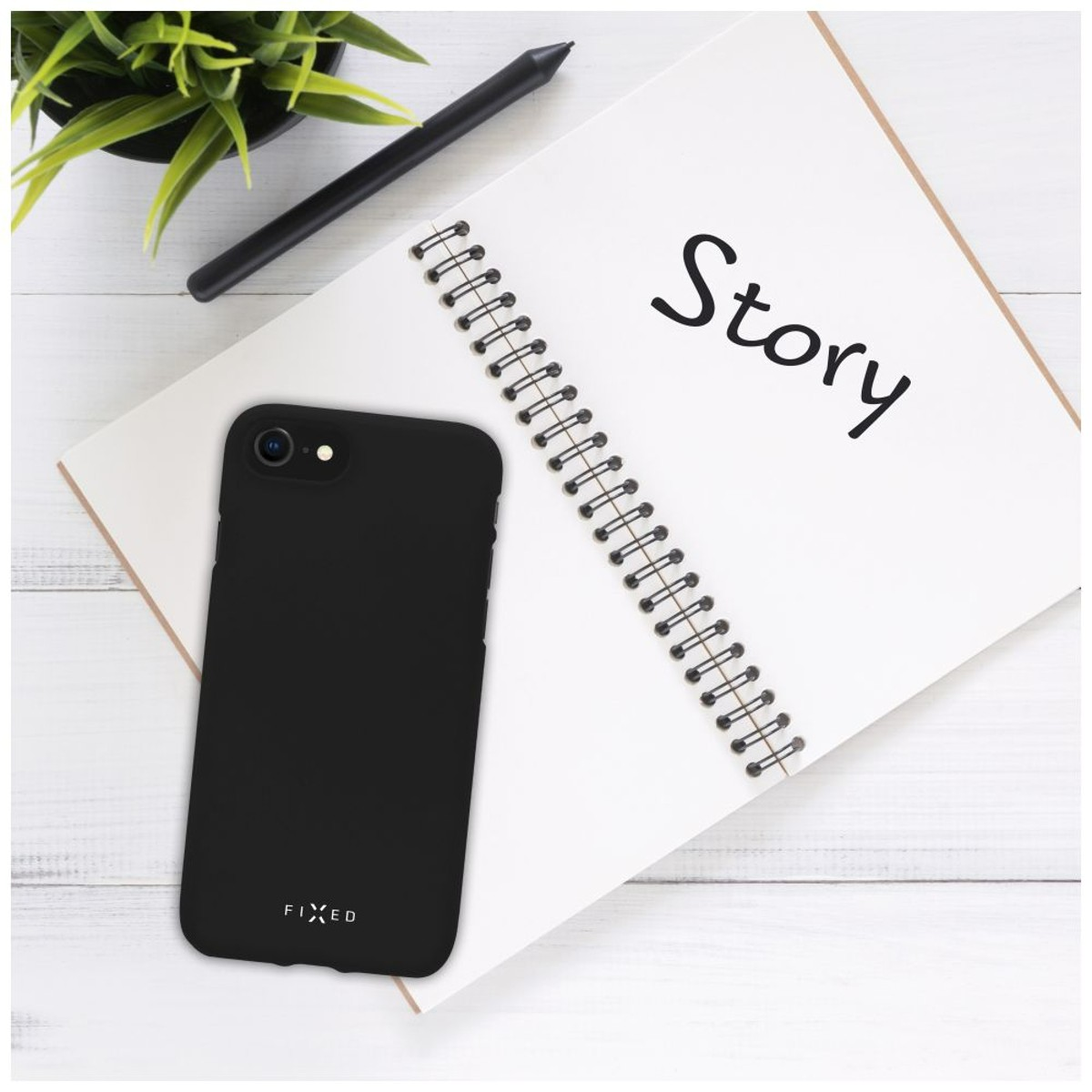 Schwarze Handyhülle, Notizbuch mit „Story“ darauf und Stift auf weißer Holzoberfläche.