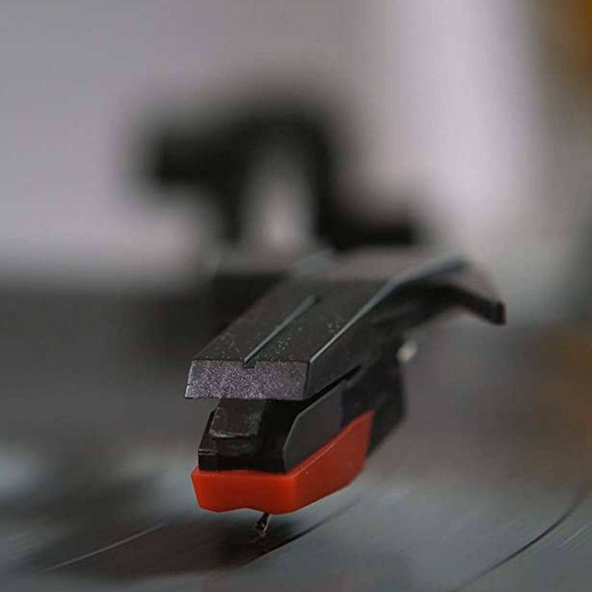 Primer plano de una aguja de tocadiscos con punta roja y cuerpo negro, sobre un disco.