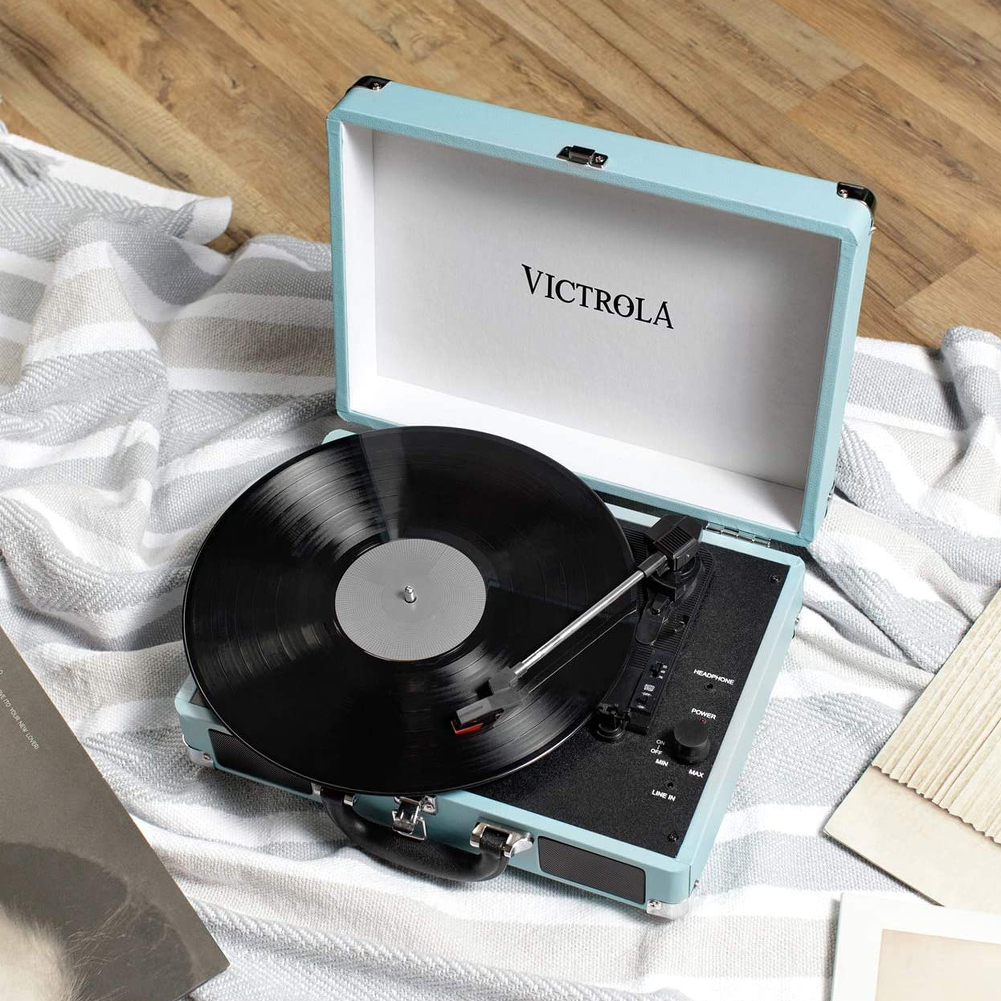 Tocadiscos con un disco negro reproduciéndose, abierto en una caja azul, sobre una superficie estampada.