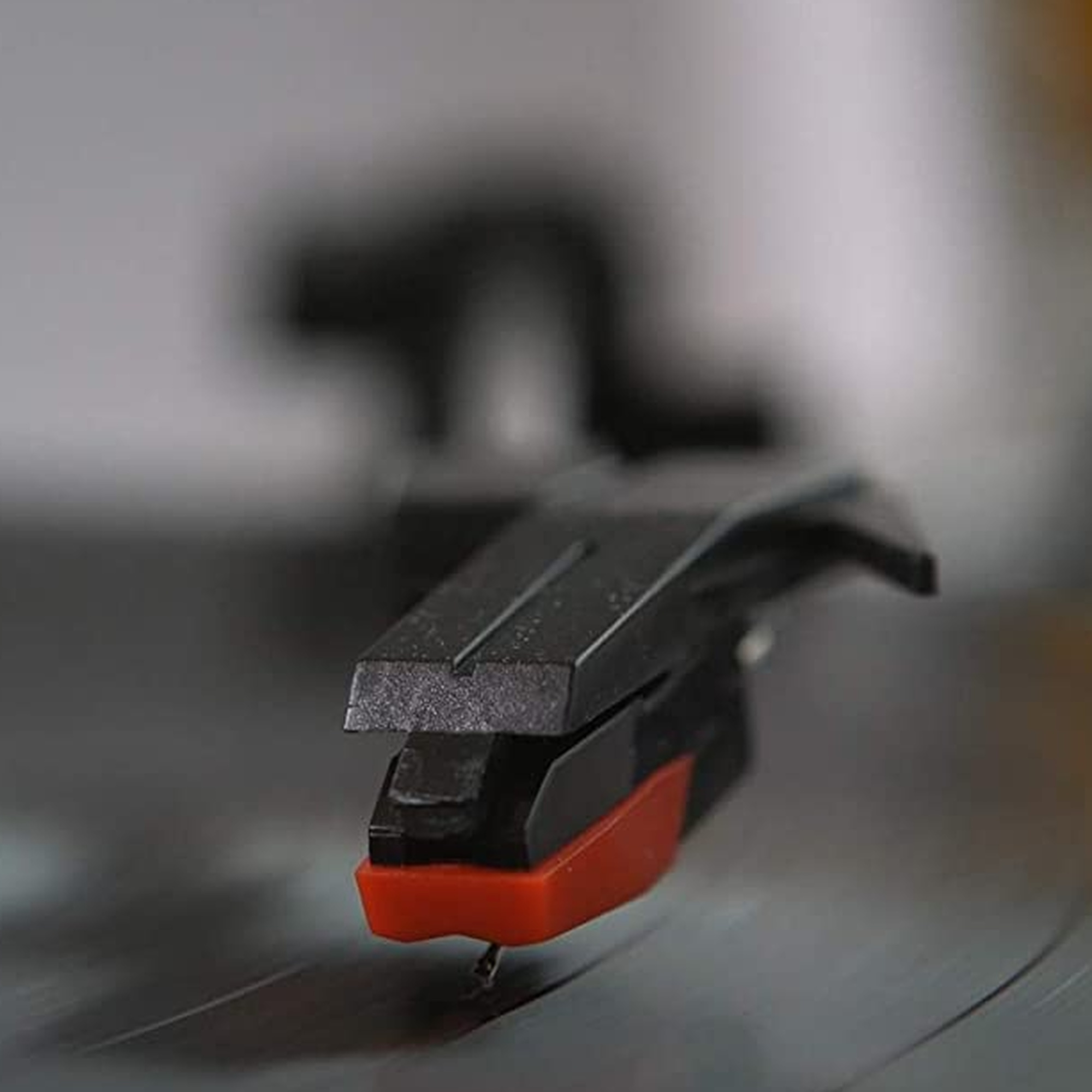 Primer plano de una aguja de tocadiscos, negra con punta roja, sobre un disco.