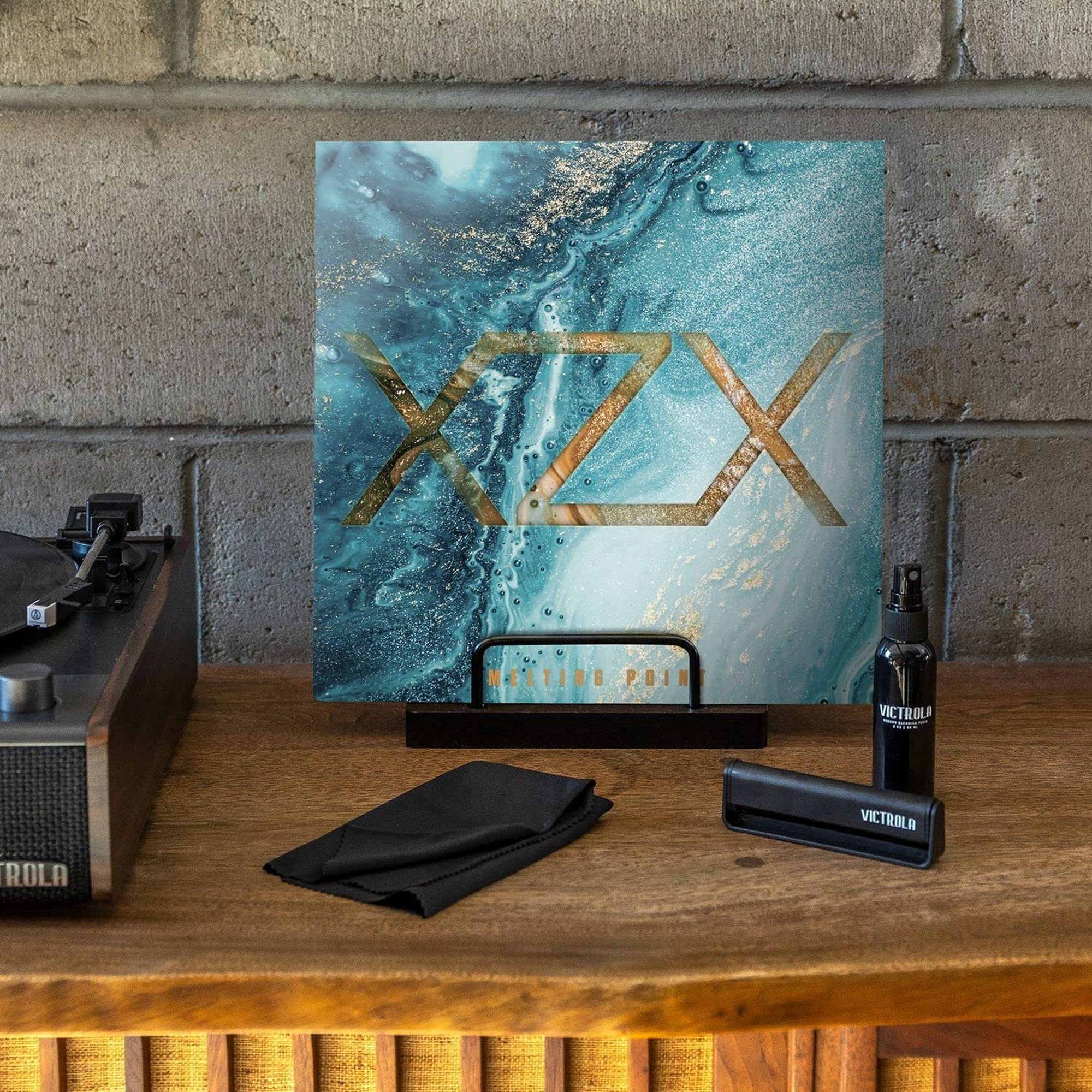 Tocadiscos con disco de vinilo, productos de limpieza y un póster sobre una superficie de madera.
