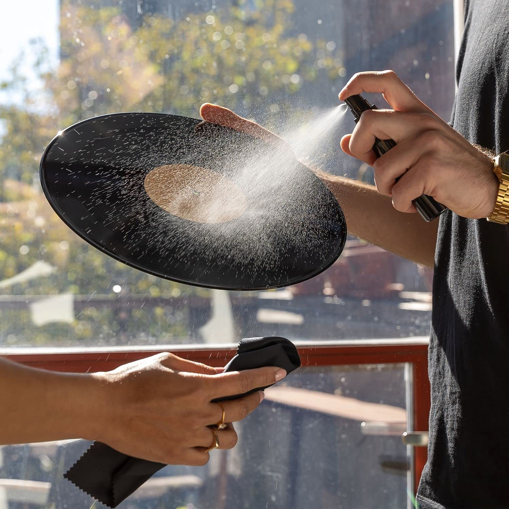 Dos manos rociando un disco de vinilo con un spray de limpieza.
