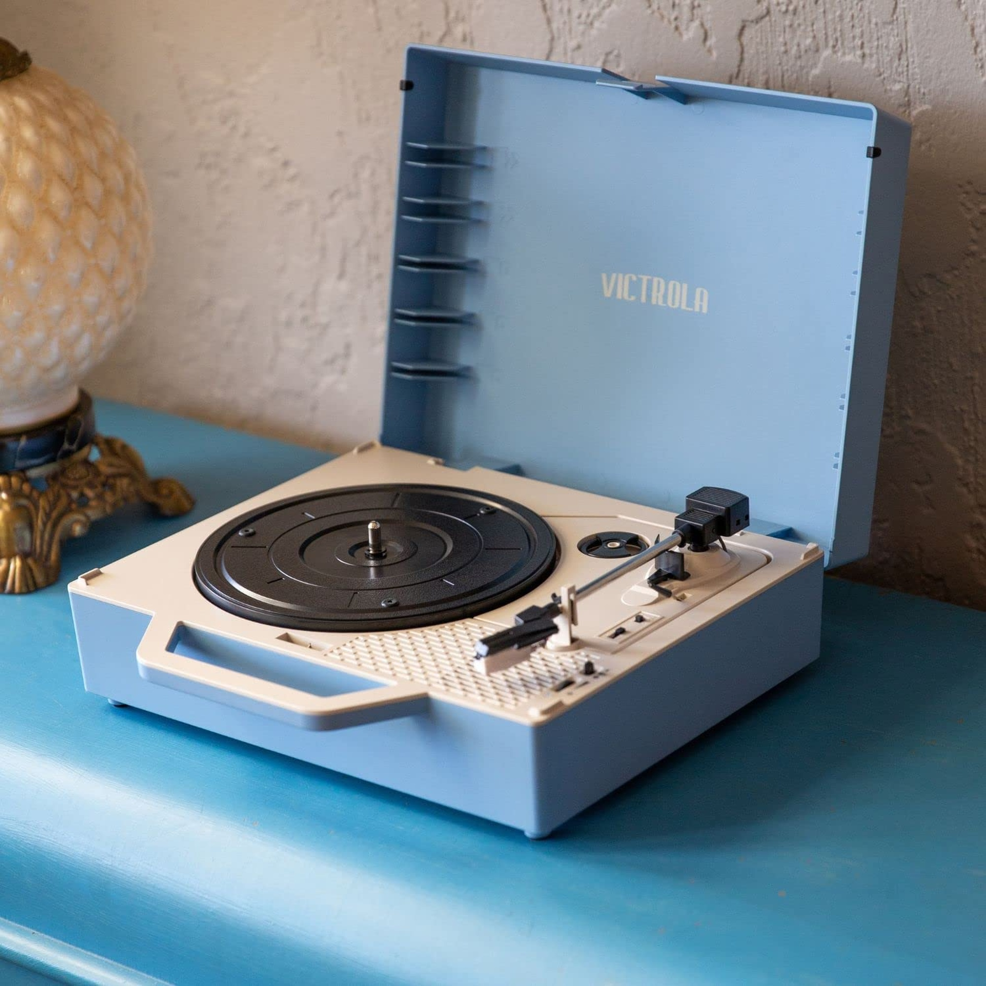 Tocadiscos Victrola azul y blanco con tapa abierta, sobre una mesa azul.