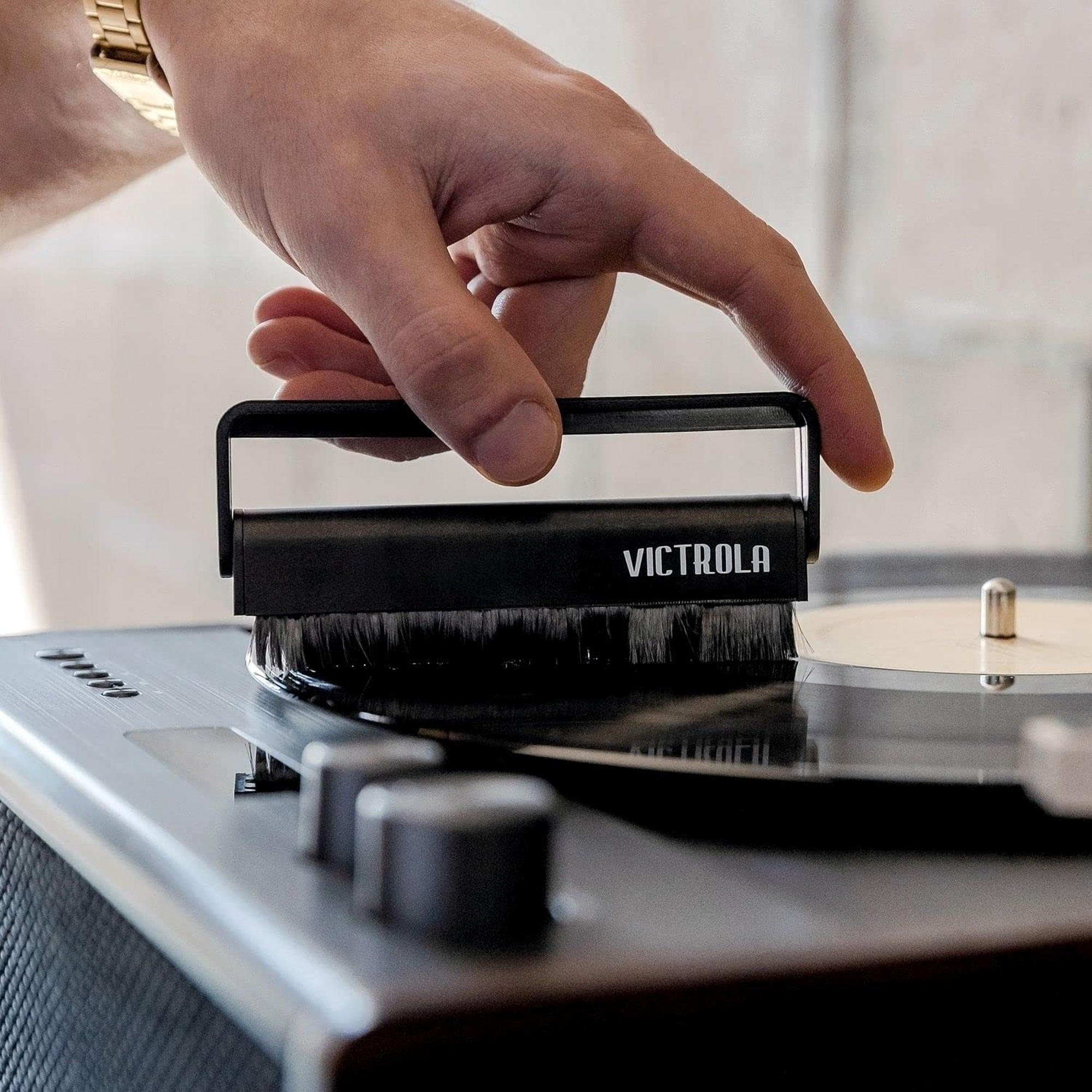 Una mano limpiando un disco de vinilo con un cepillo en un tocadiscos, mostrando la marca Victrola.