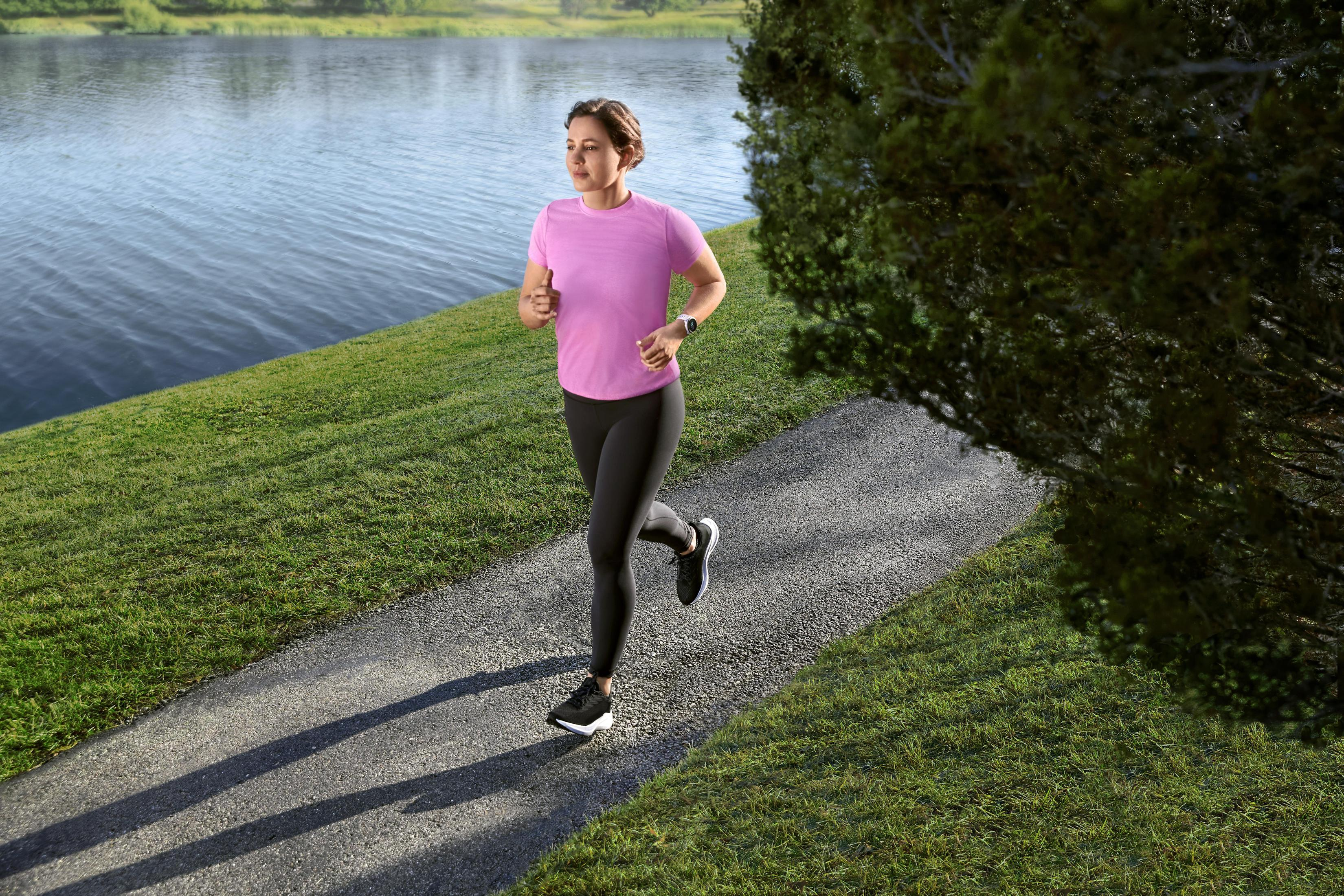Kobieta biegnąca ścieżką nad jeziorem, w różowej koszulce i czarnych legginsach.