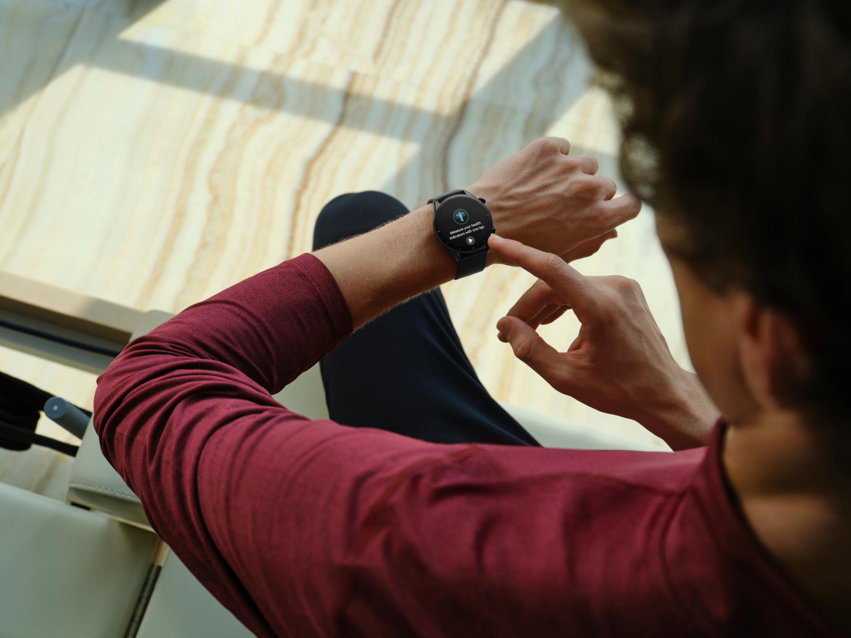 Mann checkt seine Smartwatch in Innenräumen. Die Uhr zeigt ein Display. Verschwommener Hintergrund.
