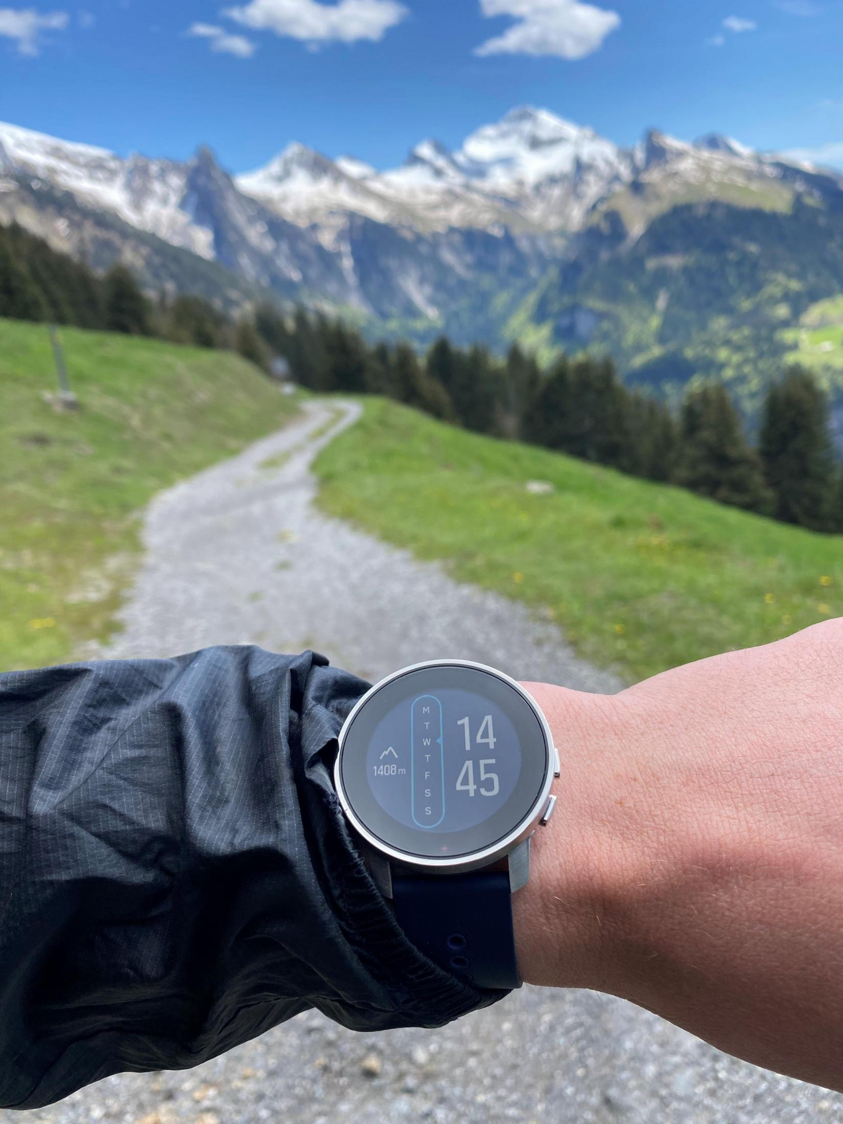 Muñeca con smartwatch, camino y paisaje montañoso.