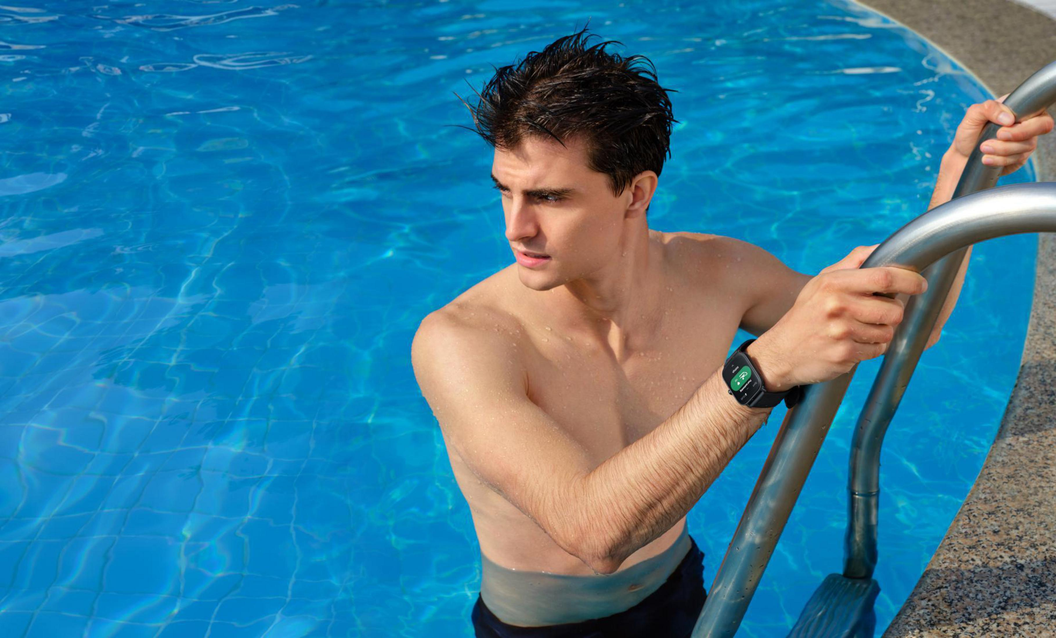 Mann im Pool, hält Leiter, schaut weg. Blaues Wasser, Sonnenlicht und eine Uhr.