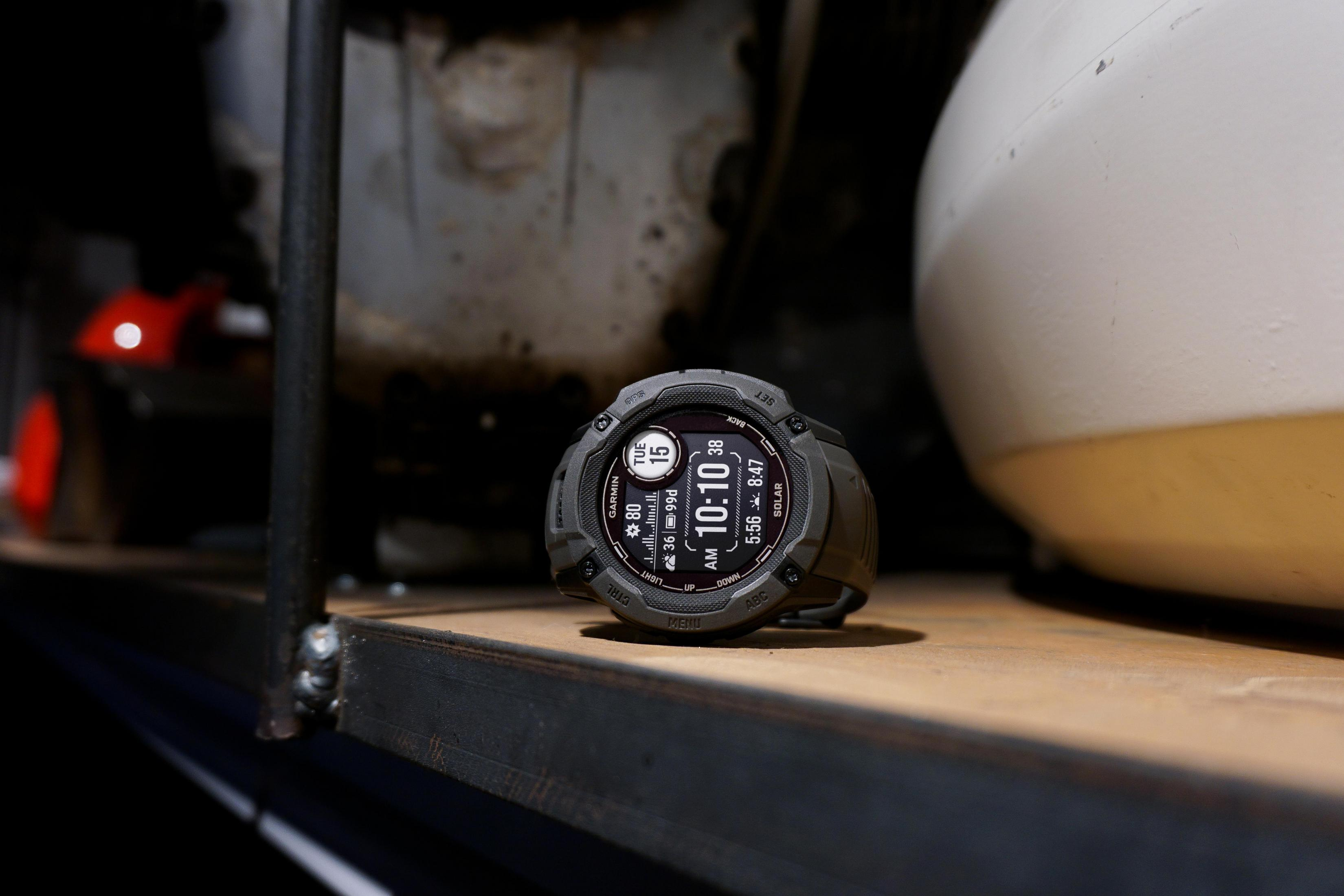 Szary smartwatch wyświetlający godzinę, datę i statystyki, na drewnie.