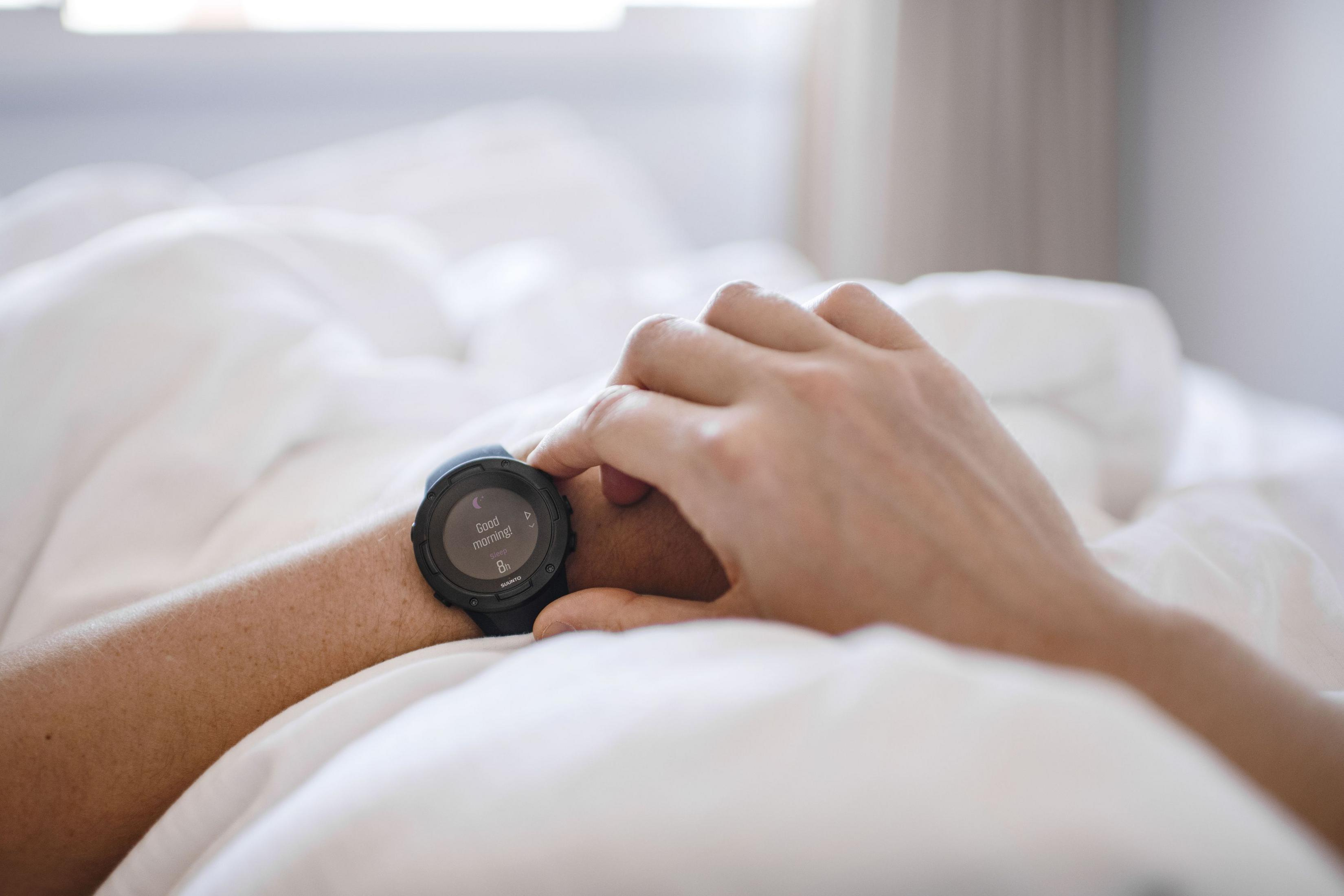 Person im Bett, die auf eine Smartwatch schaut, auf deren Bildschirm „Guten Morgen“ steht.