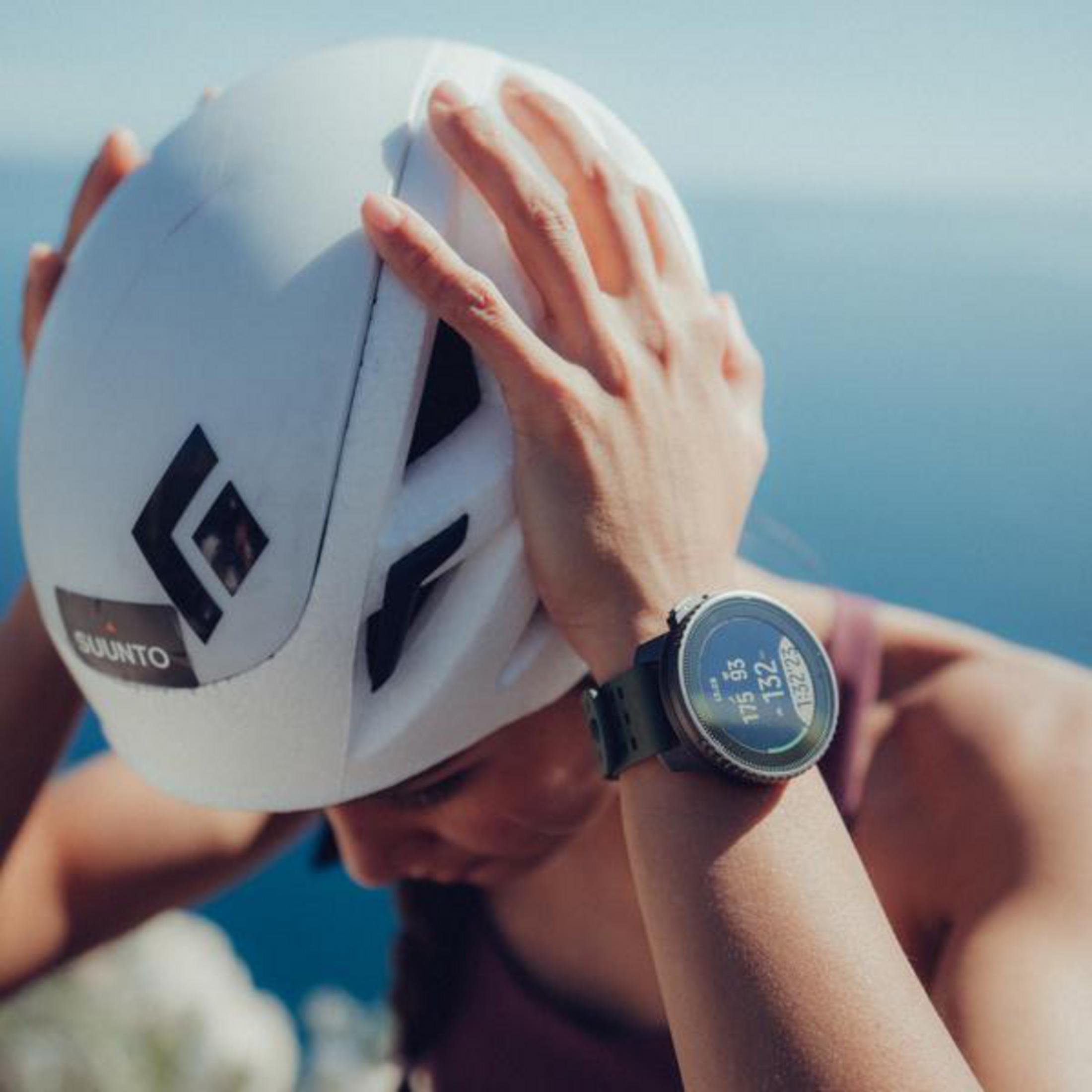 Eine Person mit Helm und Suunto-Uhr. Uhr zeigt Daten an. Blauer Hintergrund.