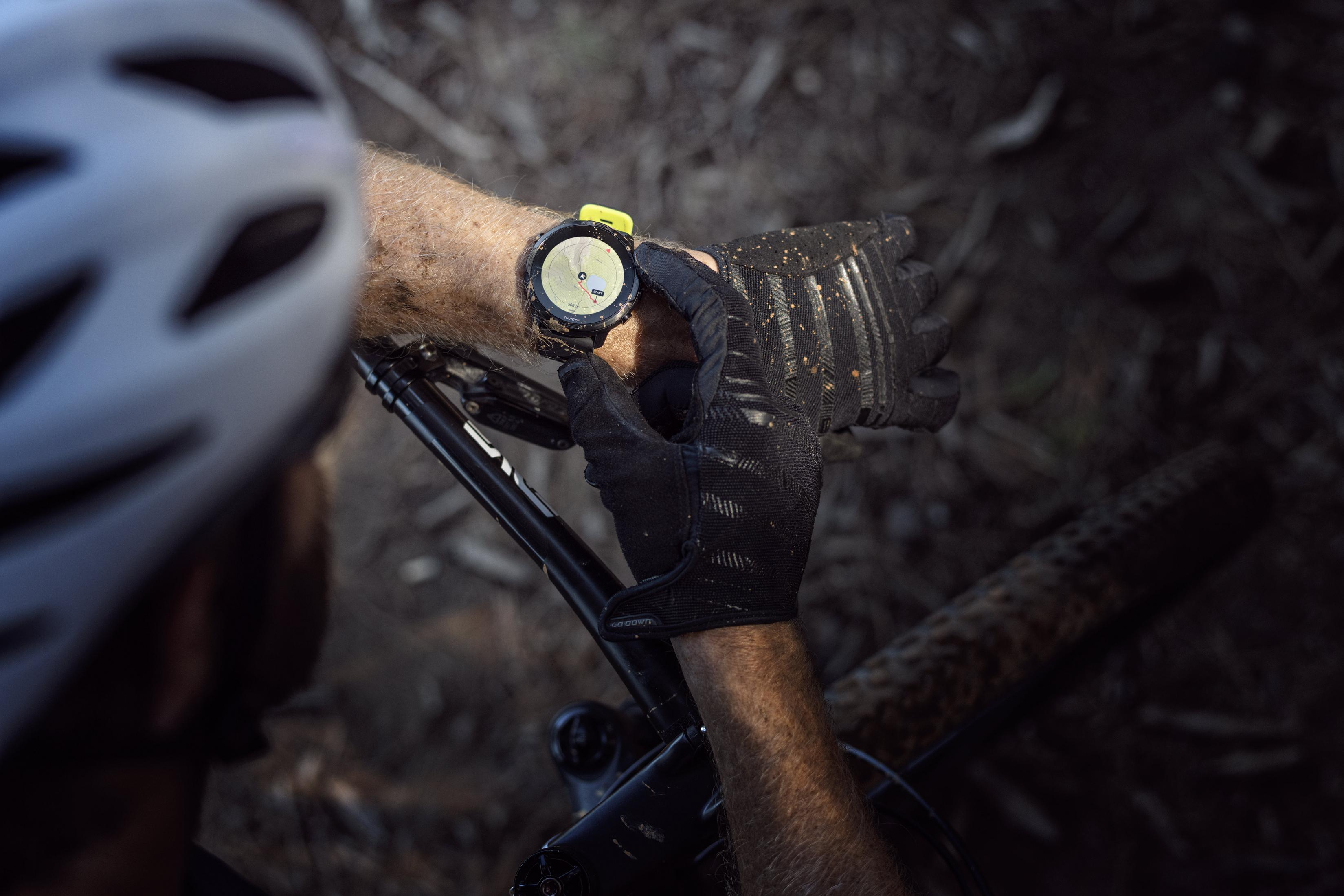 Eine Person mit Helm und Handschuhen überprüft eine Uhr am Handgelenk, während sie ein Fahrrad hält.
