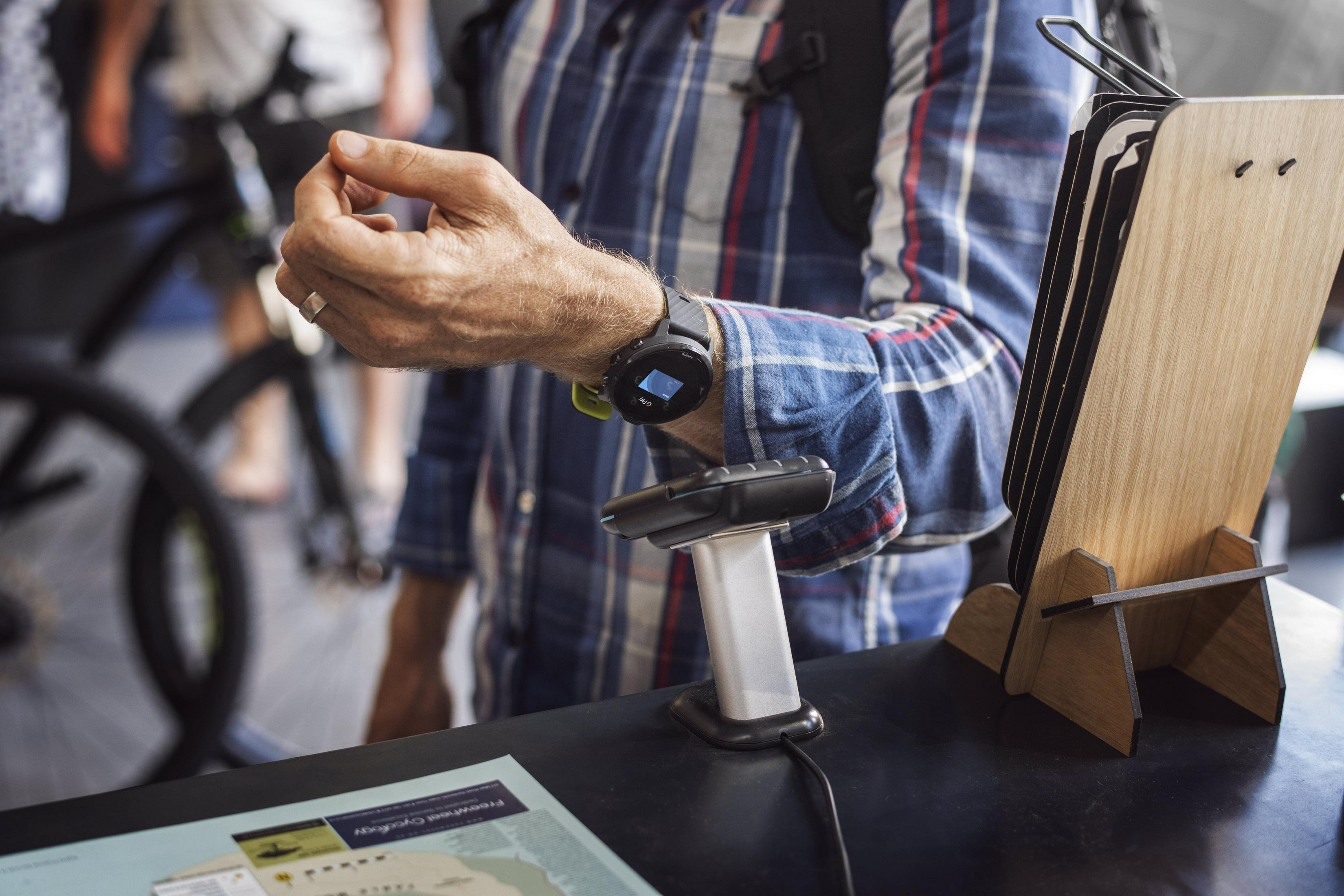 Person trägt Smartwatch, in der Nähe eines Kiosks mit Scanner und gedrucktem Dokument.