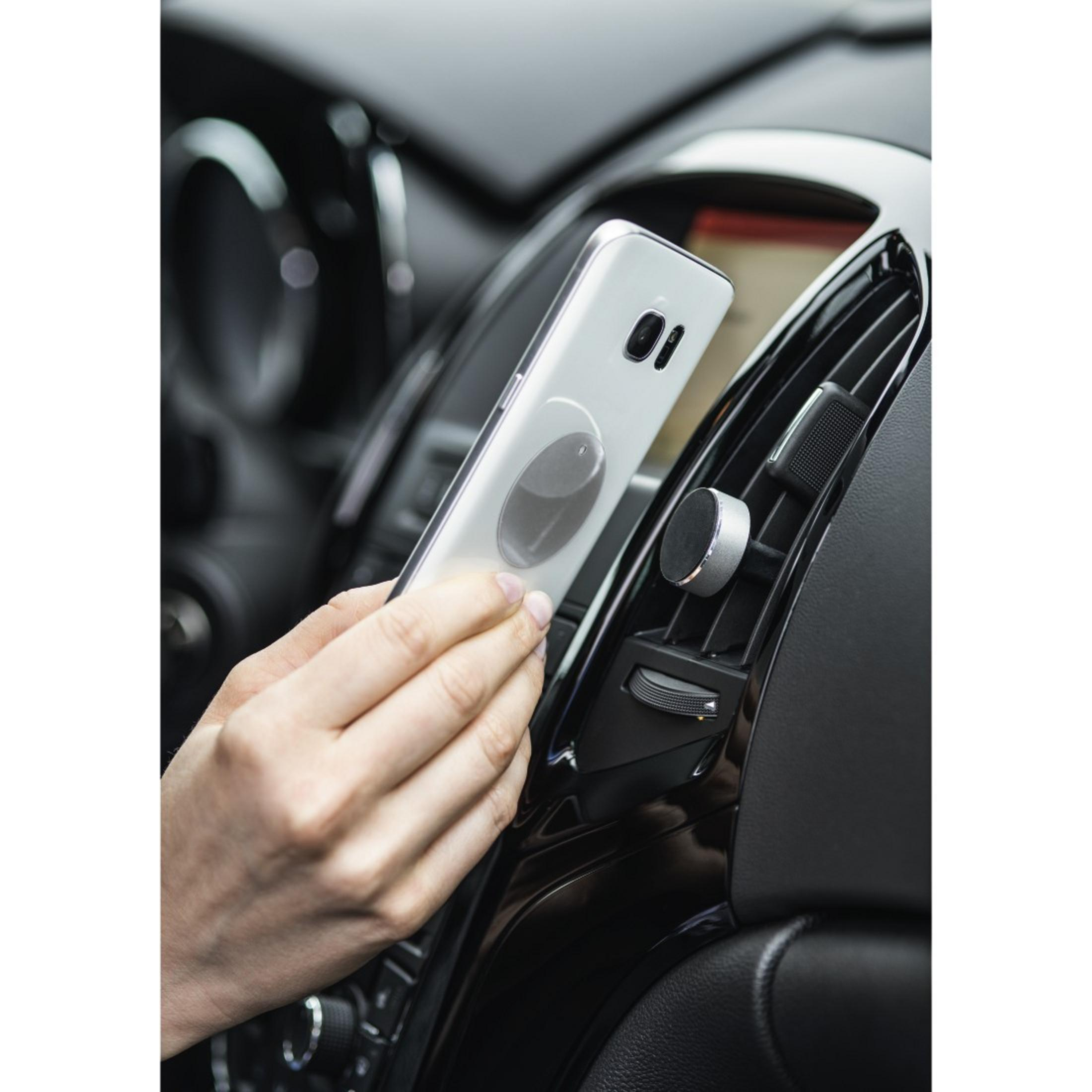 Dłoń trzyma srebrny telefon przy wylocie powietrza w samochodzie, czarne wnętrze.