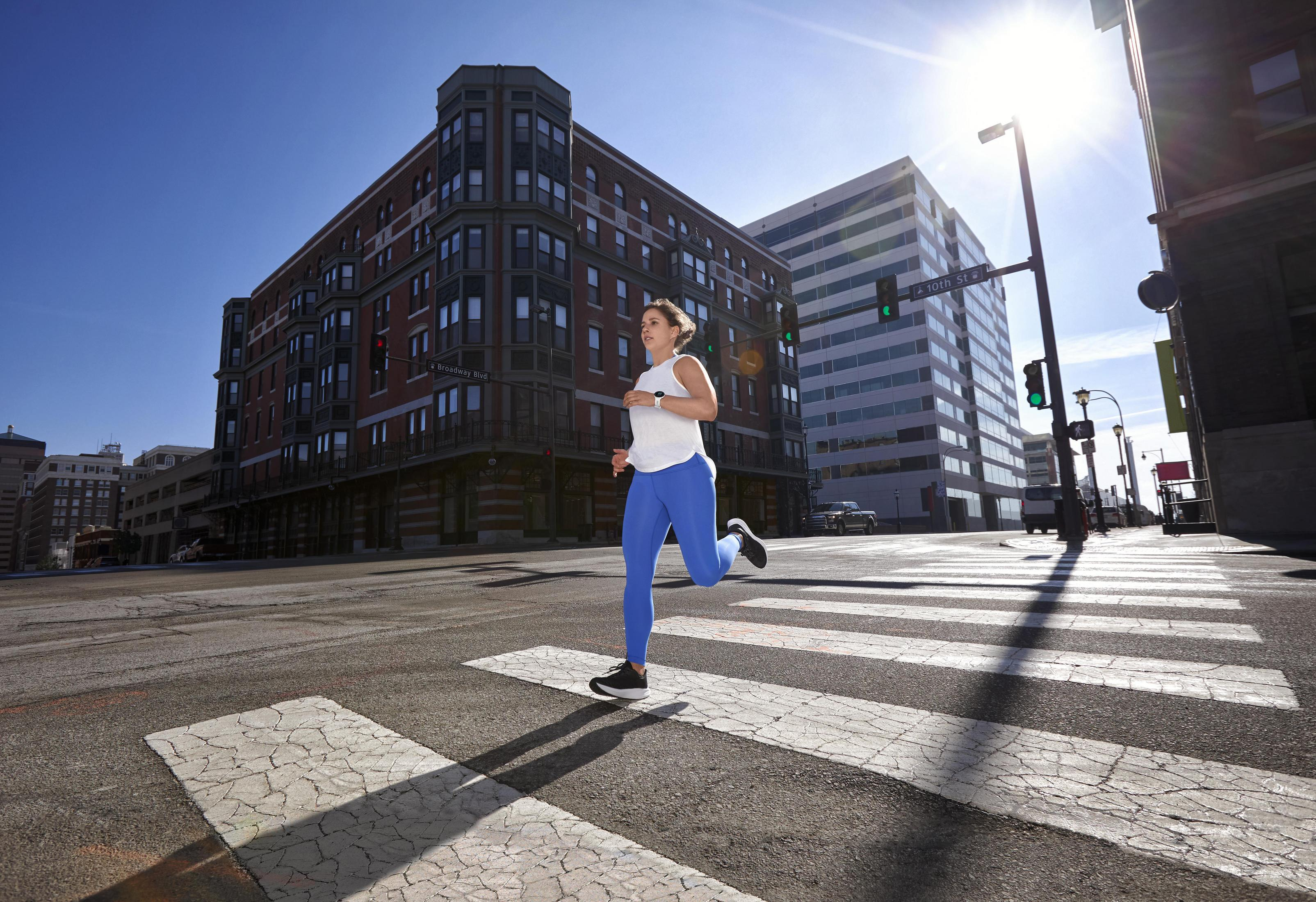Mujer corriendo por un paso de peatones frente a un edificio. El cielo es azul y el sol brilla.