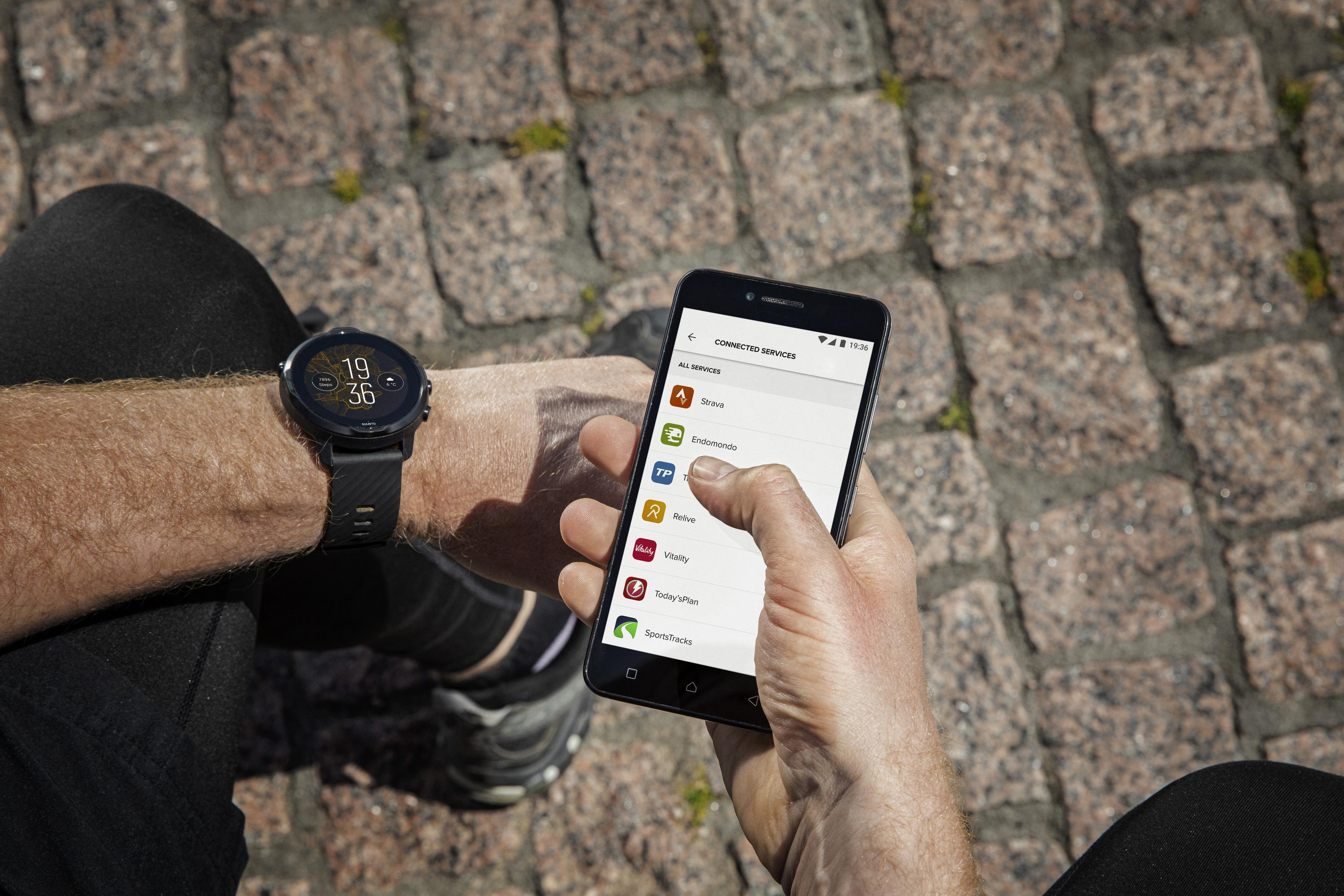 Person schaut auf Smartwatch und Smartphone, Kopfsteinpflasterhintergrund.