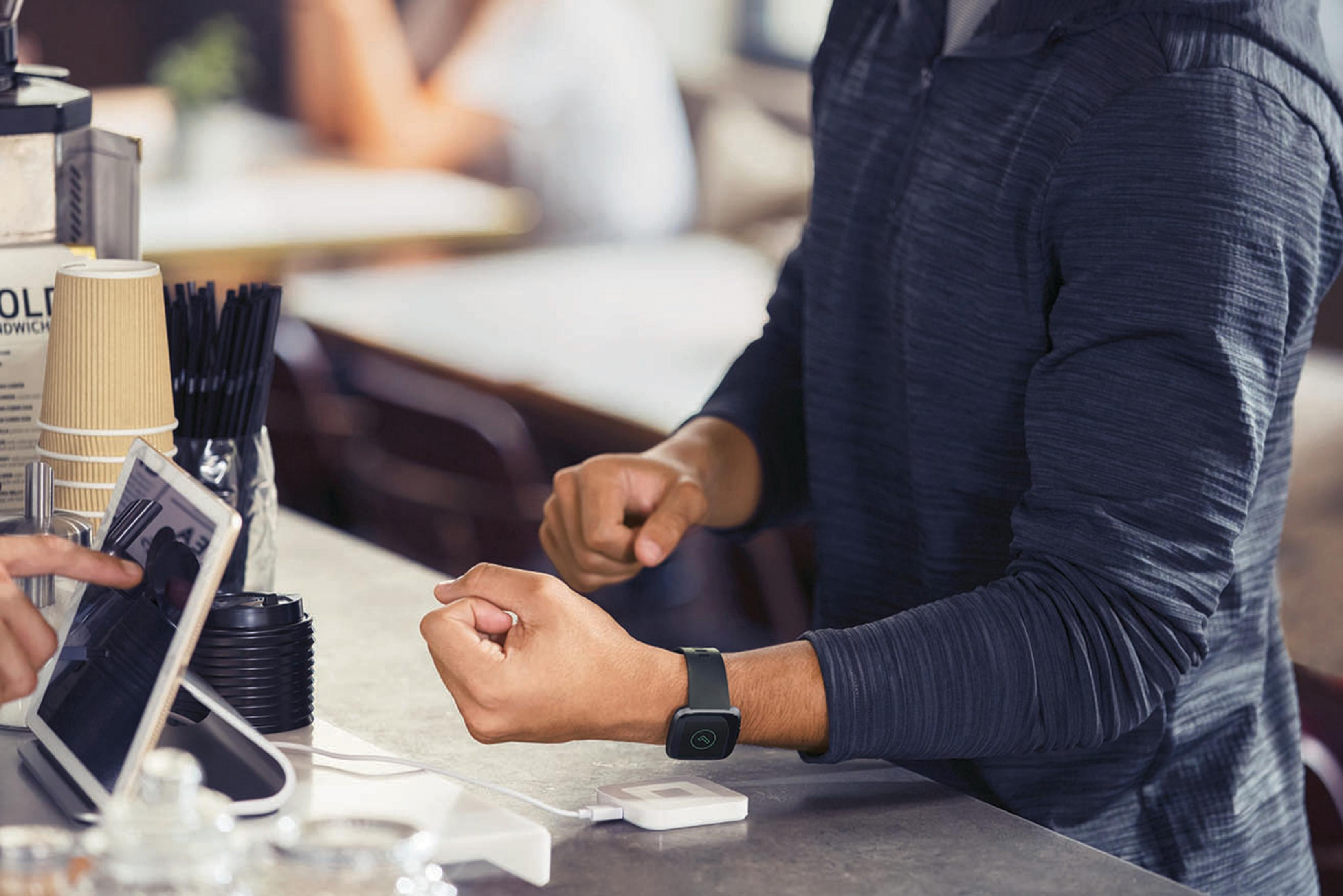 Una persona paga con uno smartwatch in un bar. Tengono il braccio vicino a un terminale di pagamento.