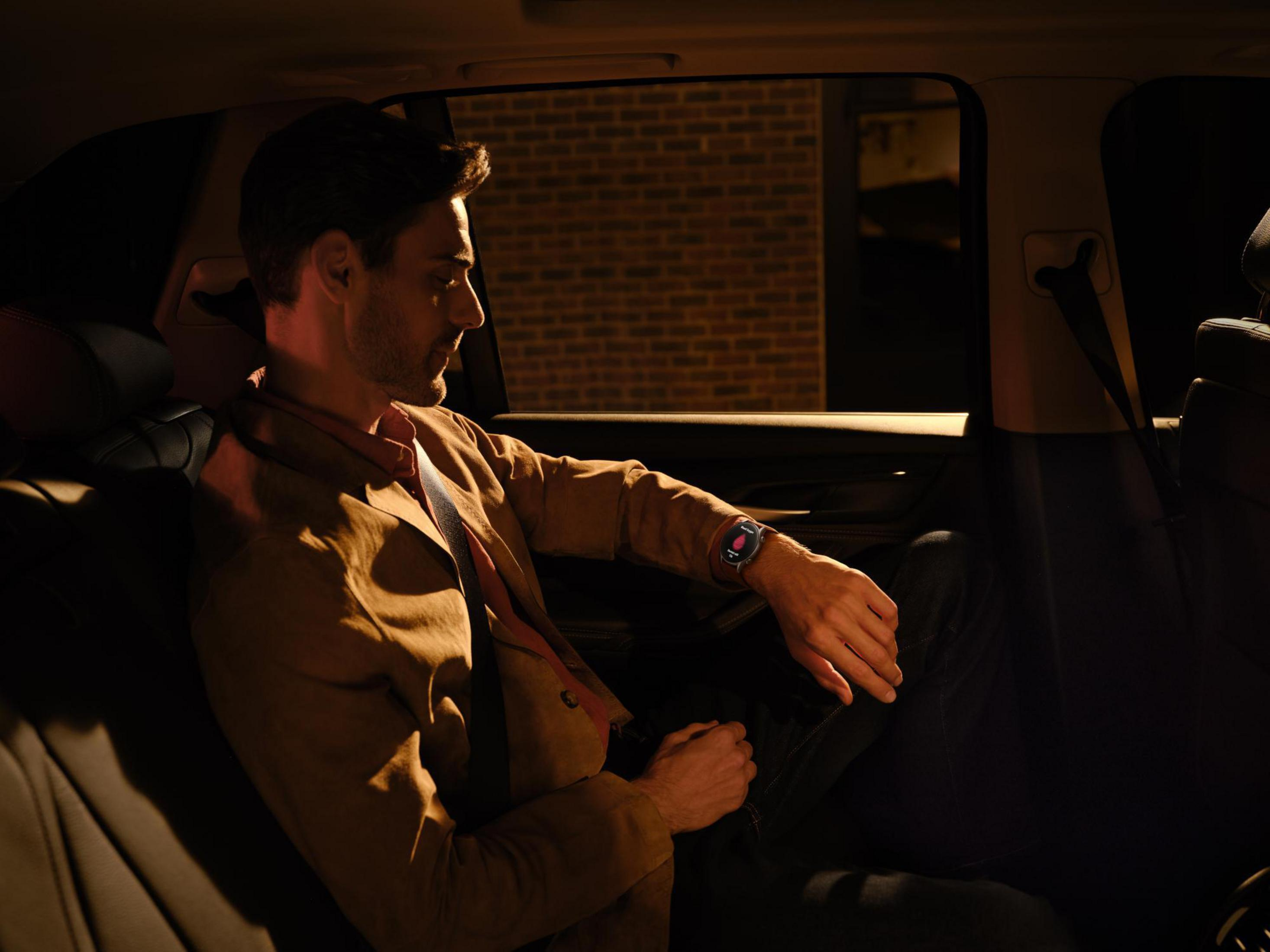 Ein Mann mit Uhr im Auto bei Nacht. Das Zifferblatt ist sichtbar. Innenraumbeleuchtung ist gedämpft.