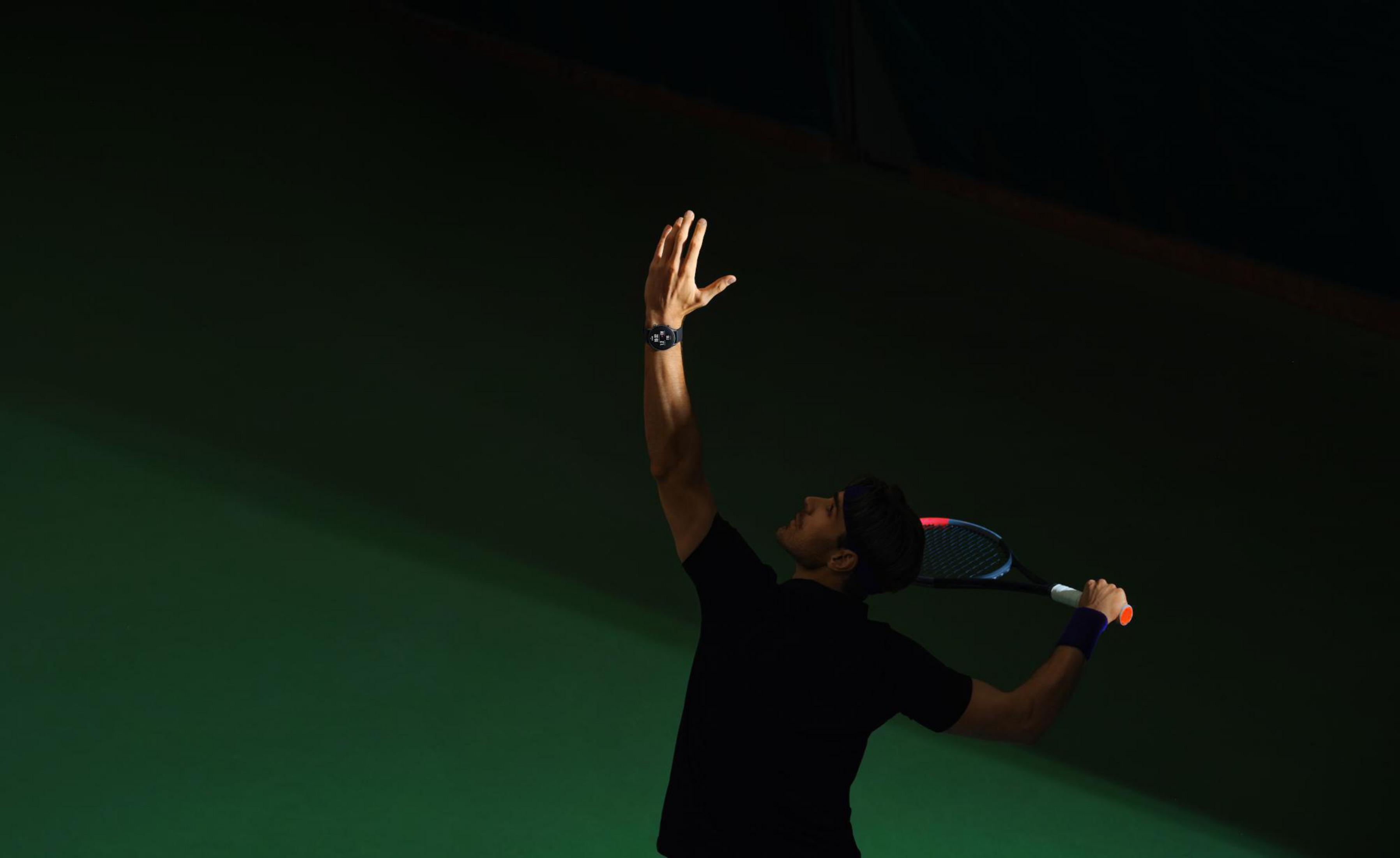 Tennisspieler in Schwarz beim Aufschlag. Grüner Hintergrund. Arm erhoben und Schläger zurück.