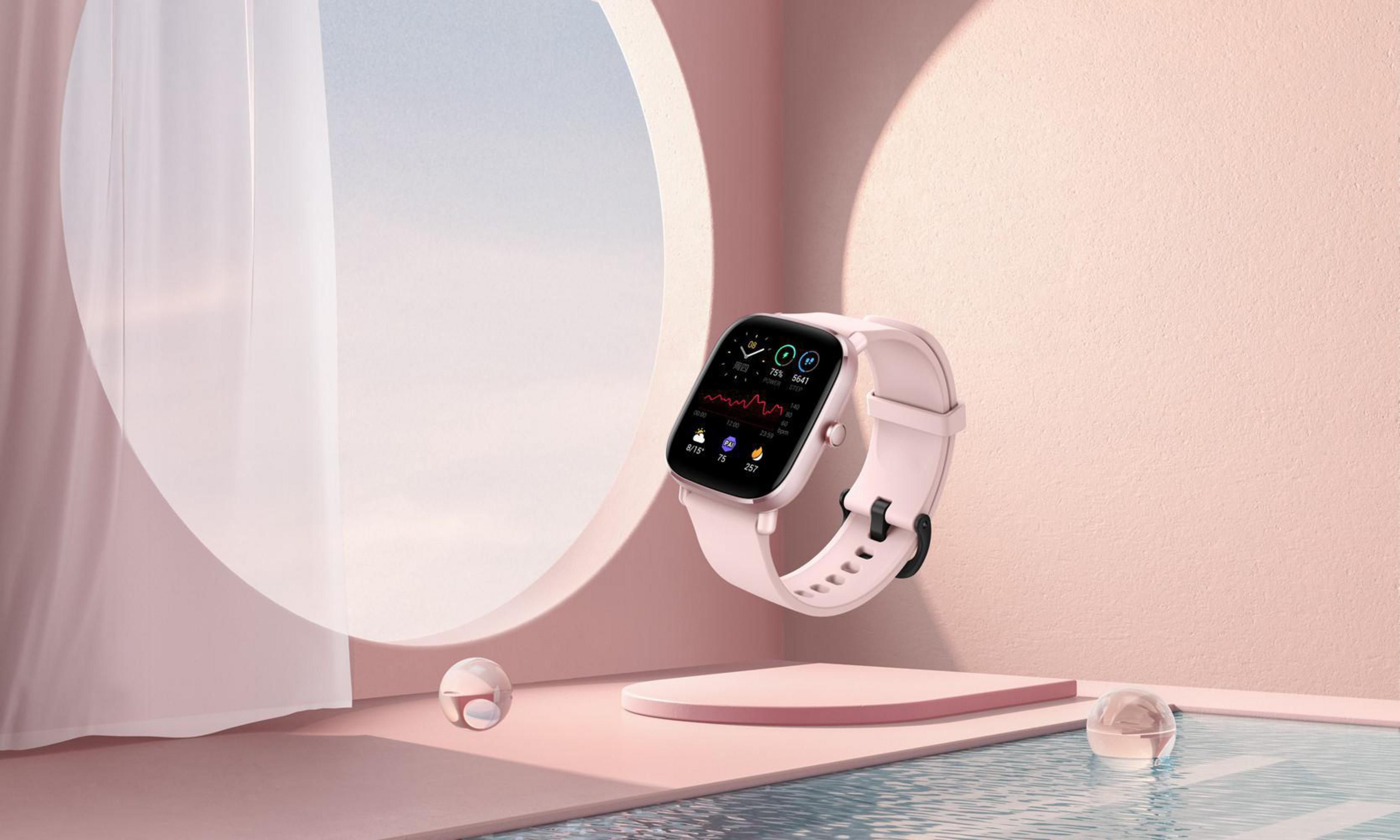 Uno smartwatch rosa con cinturino bianco, fluttuante di fronte a uno sfondo rosa con un ritaglio circolare.