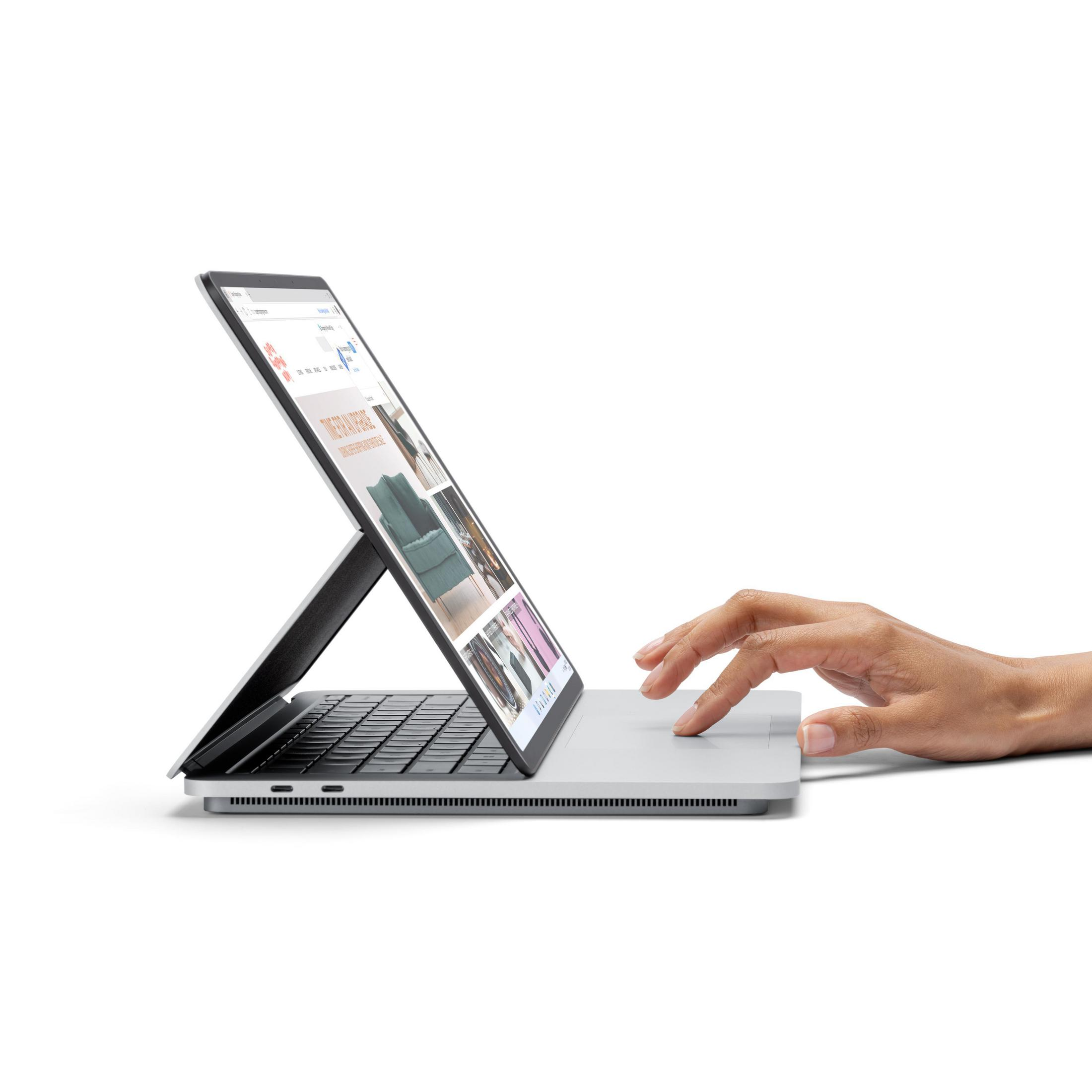 Laptop auf weißer Oberfläche, angewinkelt geöffnet. Eine Hand berührt das Trackpad. Webseite sichtbar.