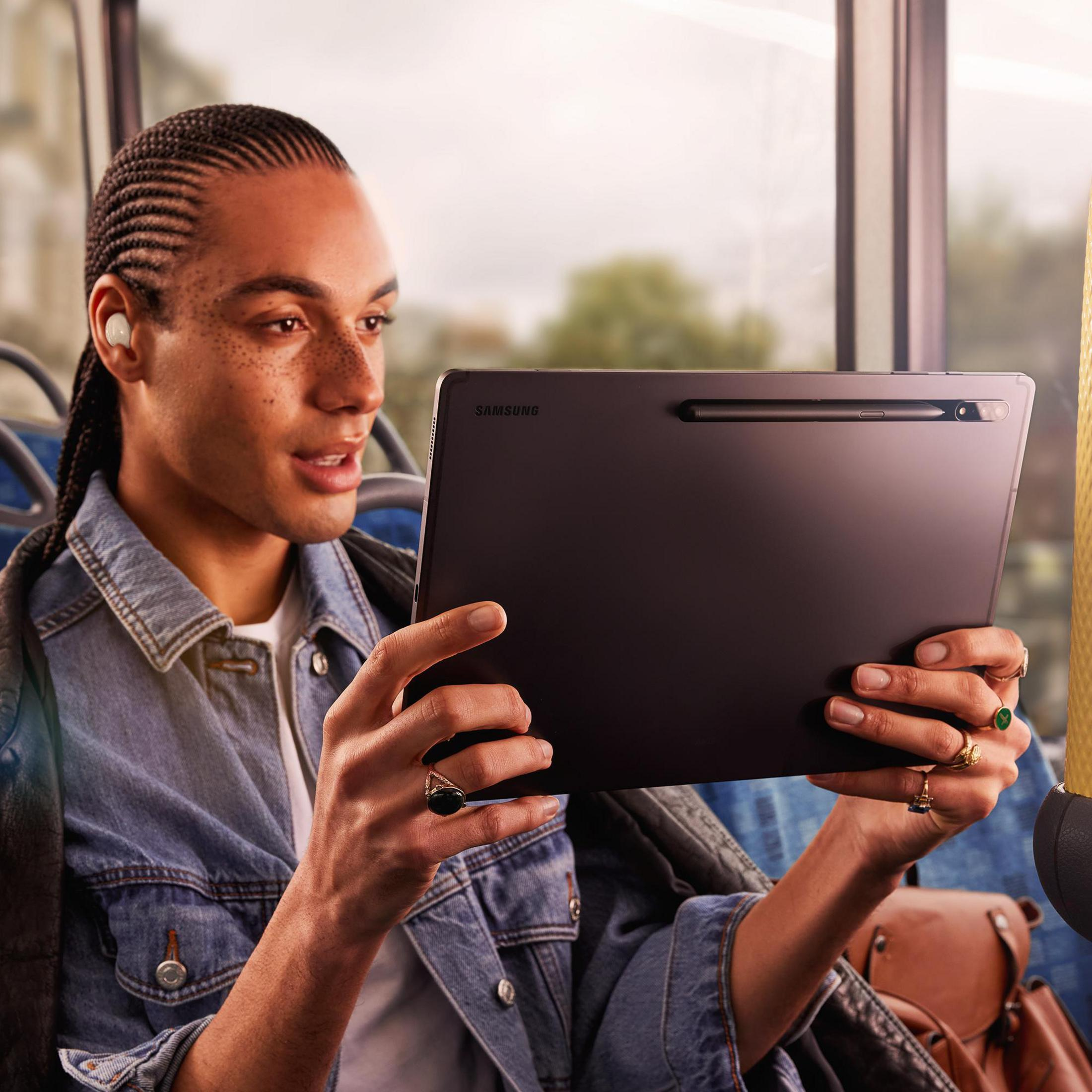 Ein Mann benutzt ein Tablet im Bus, trägt Ohrhörer und hält einen Stift.