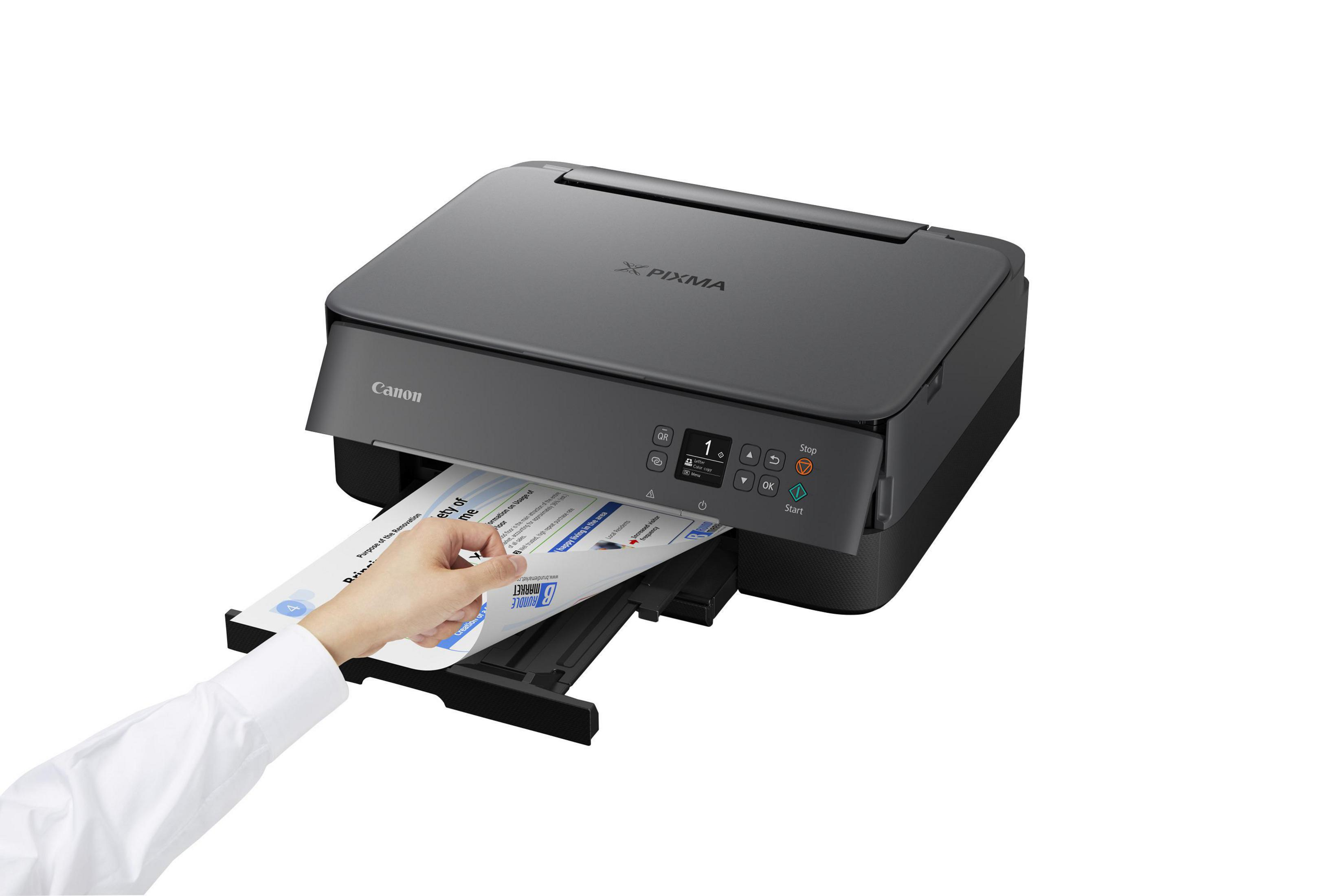 Una impresora Canon imprimiendo un documento. Una mano alcanza el papel.