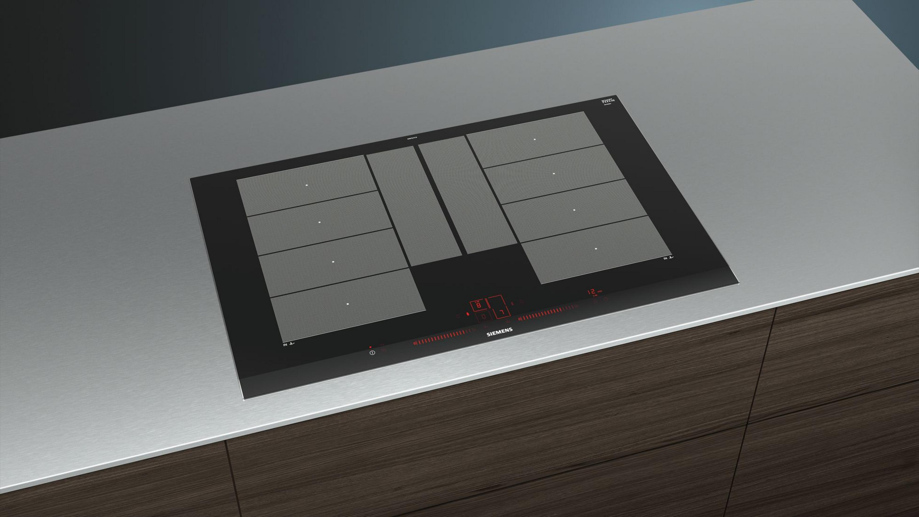 Czarna płyta grzewcza na szarej powierzchni. Ma palniki i wyświetlacz cyfrowy. Tło jest brązowe.