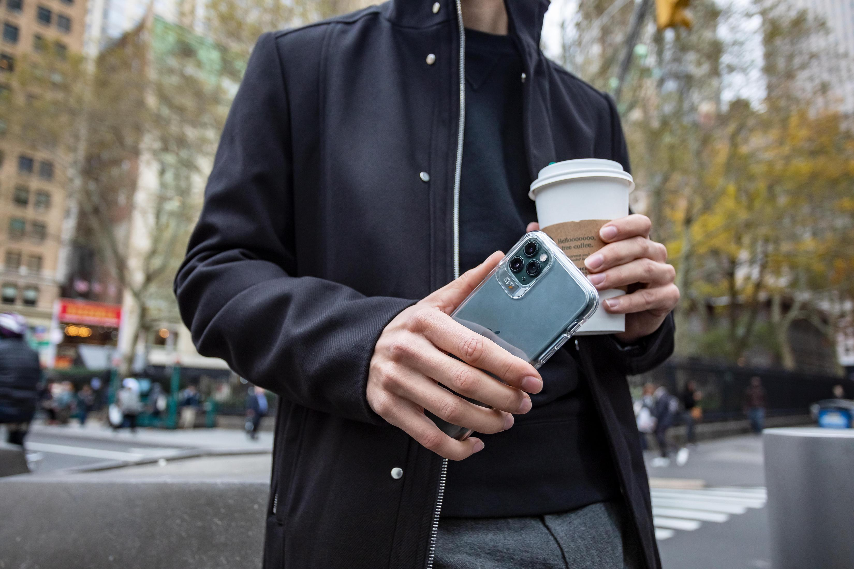 Uomo che tiene un telefono in una custodia trasparente e una tazza di caffè in strada.