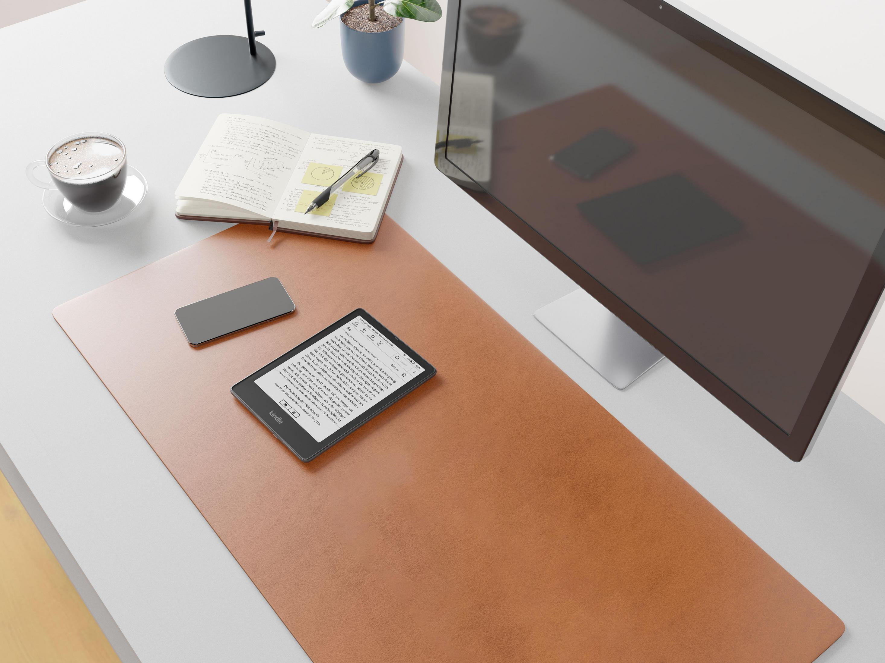 Schreibtisch mit Notizbuch, Telefon, E-Reader und Computermonitor. Braune Schreibtischunterlage.