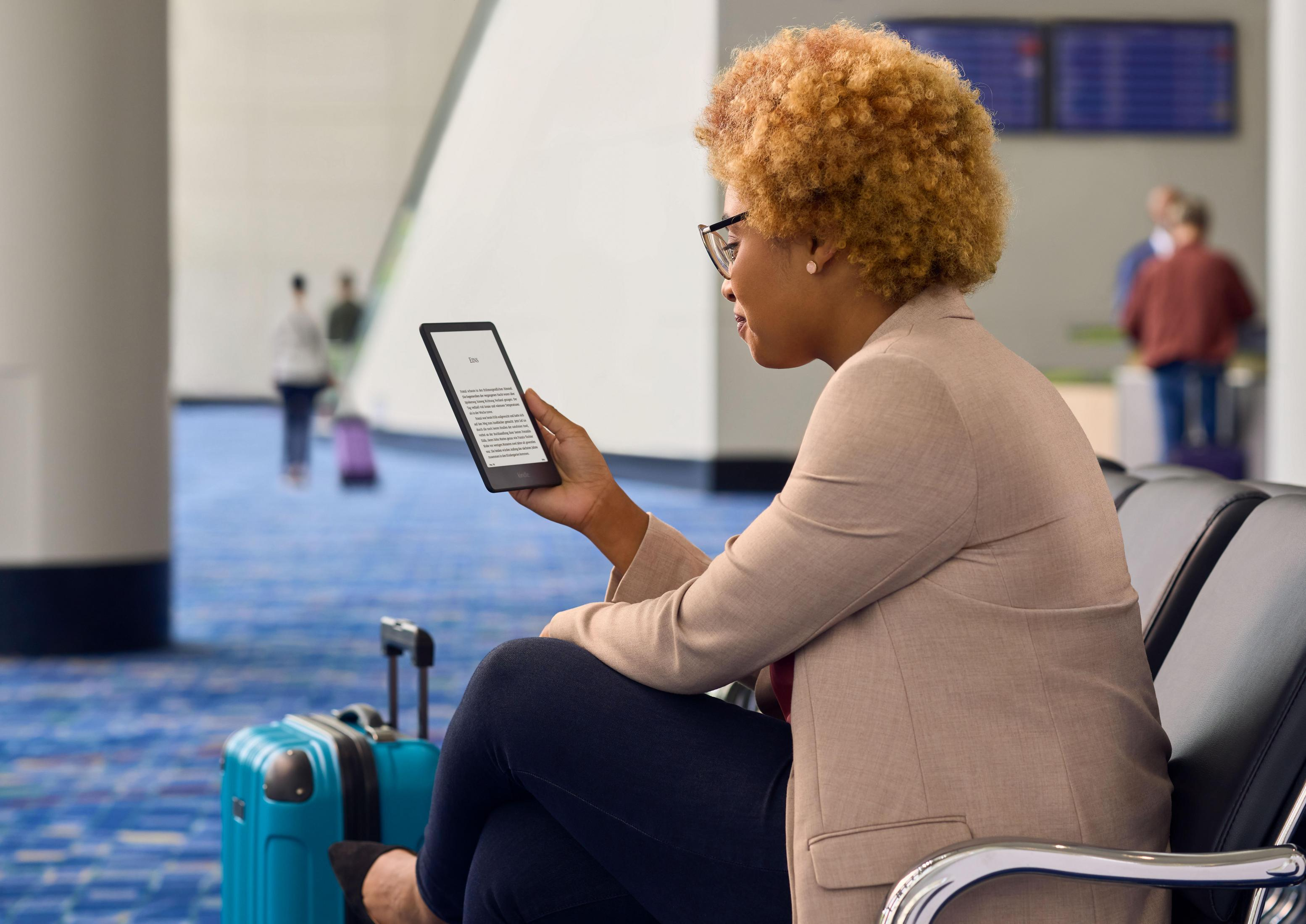 Frau mit Brille liest E-Reader am Flughafen, blauer Teppich und Sitze.