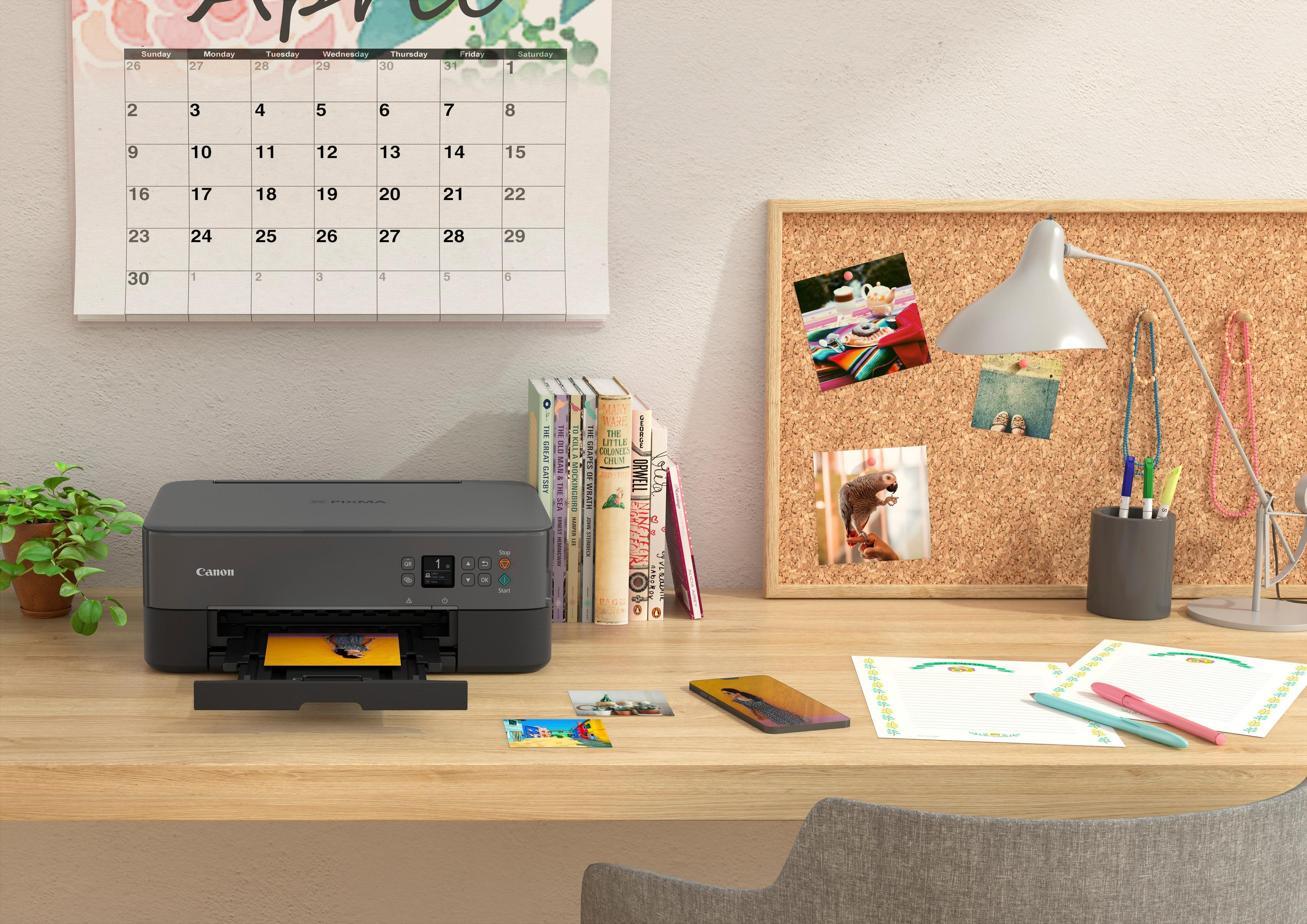 Una scrivania con una stampante, un calendario e oggetti come foto e penne.