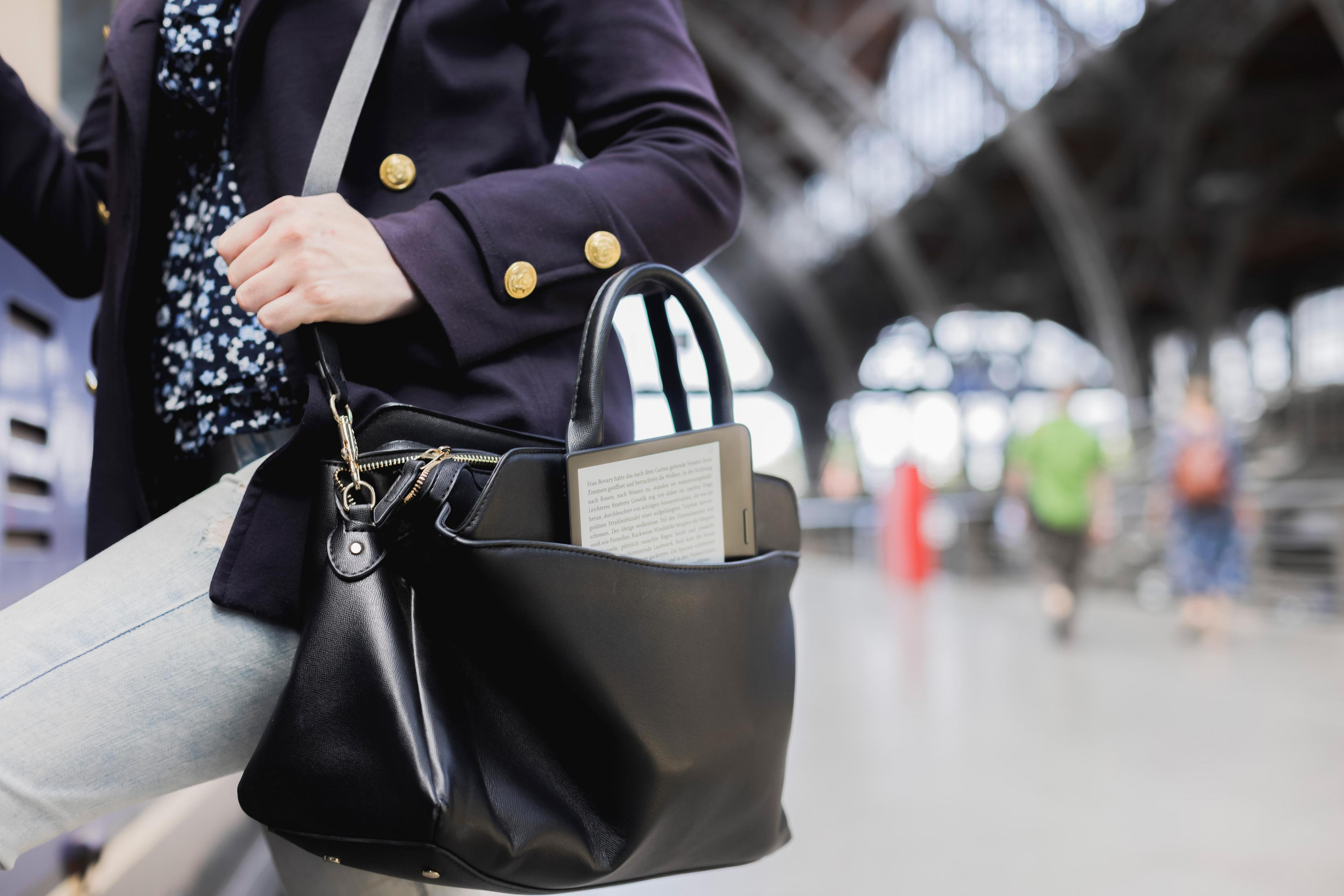 Kobieta niosąca czarną torbę z tabletem w środku, stojąca na dworcu kolejowym.
