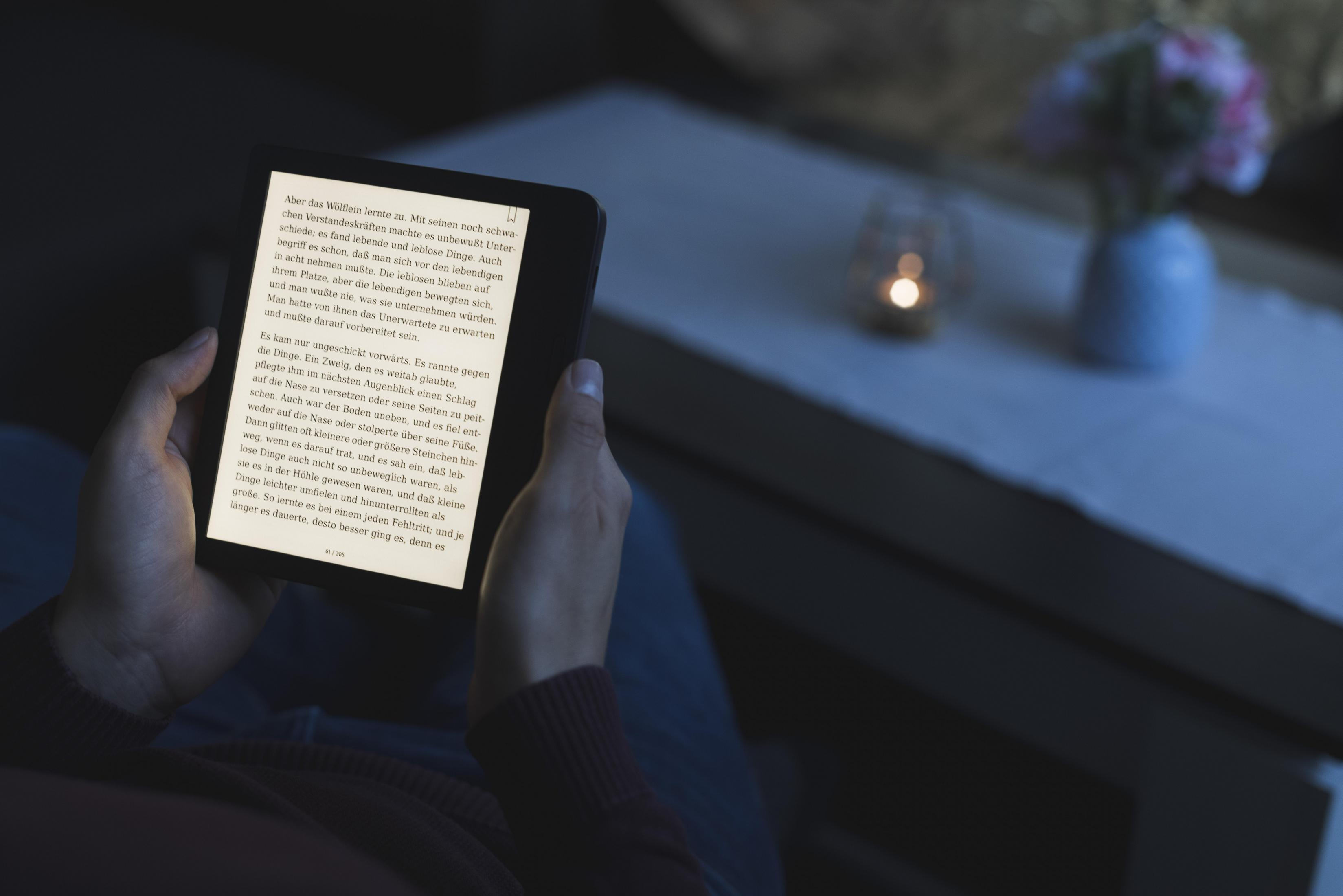 Osoba czytająca czytnik e-booków w słabym świetle, z tekstem na ekranie.