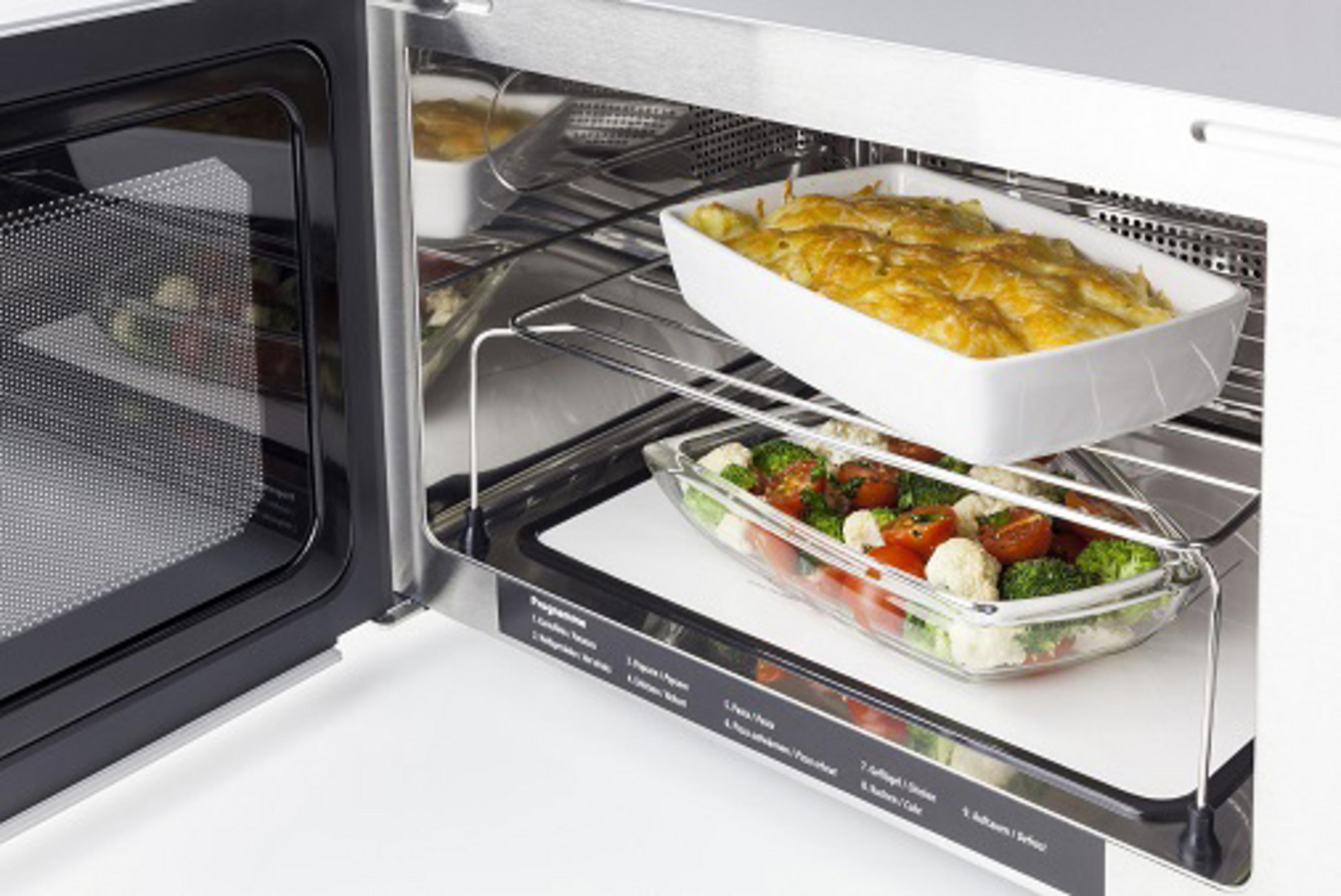 Un forno a microonde con due piatti all'interno, uno con cibo e uno con un vassoio bianco.