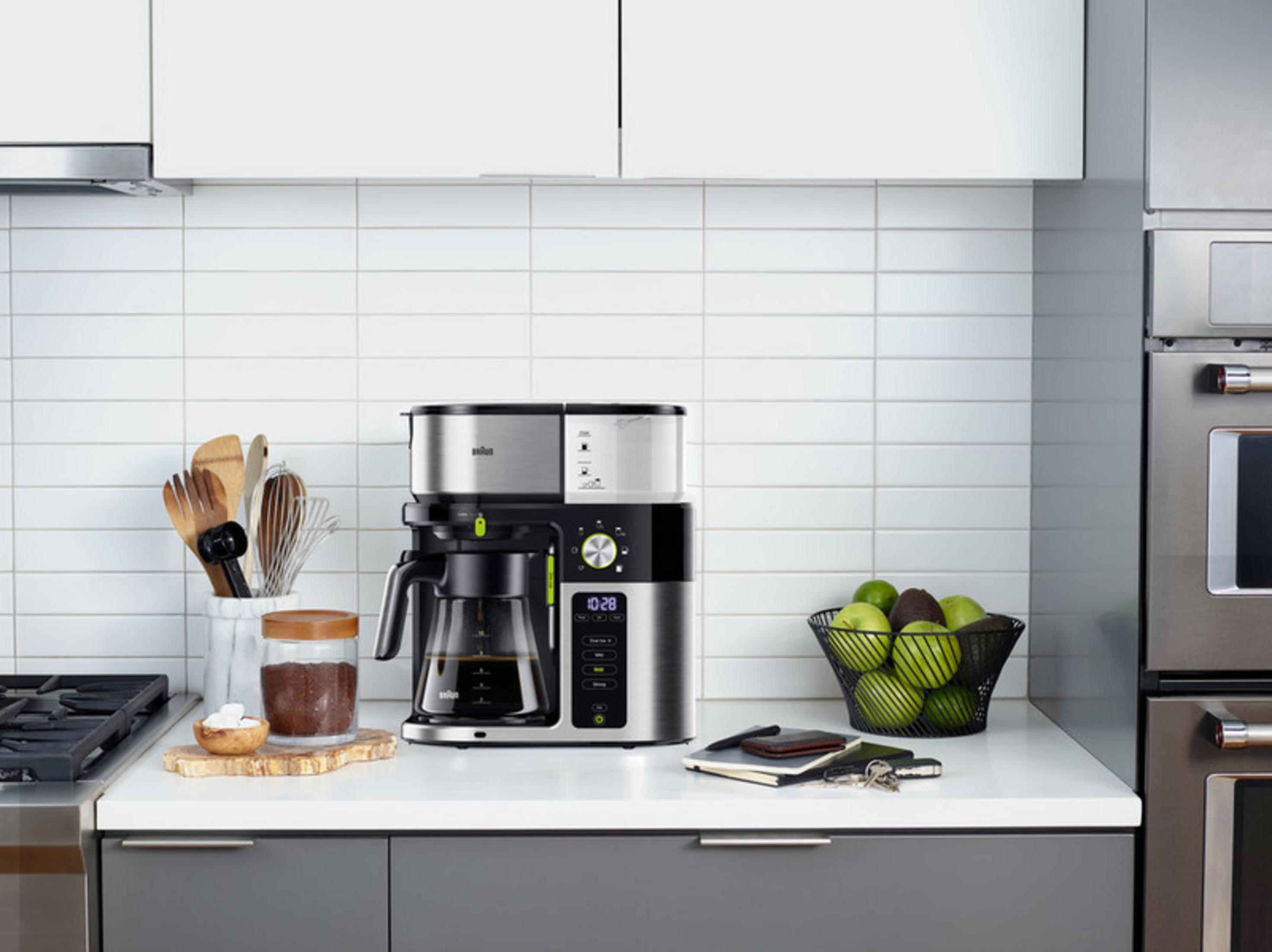 Eine moderne Küche mit Kaffeemaschine, Gläsern und frischem Obst auf einer weißen Arbeitsplatte.