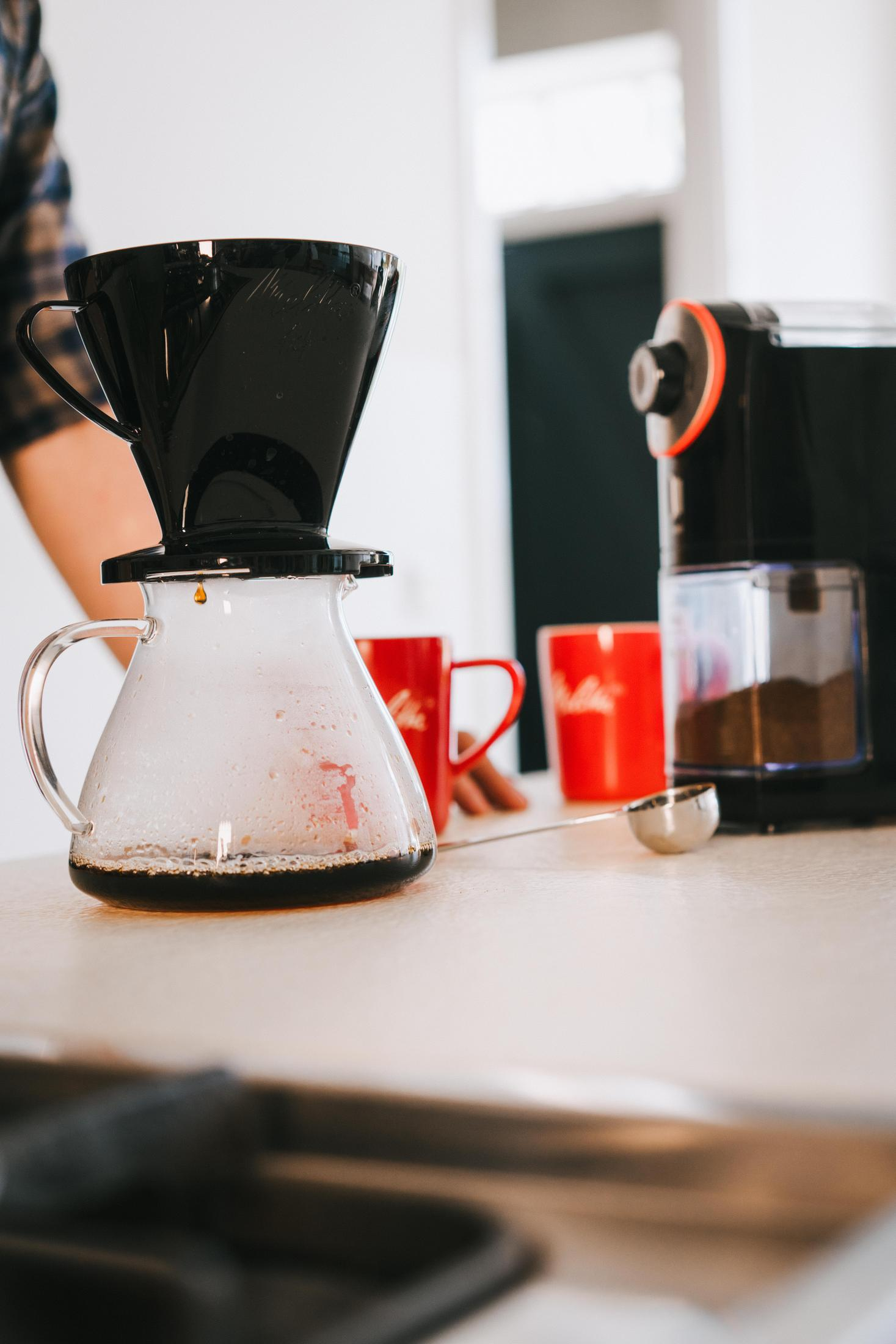 Kawa parzona w szklanej karafce z czarnym filtrem i czerwonymi kubkami na stole.