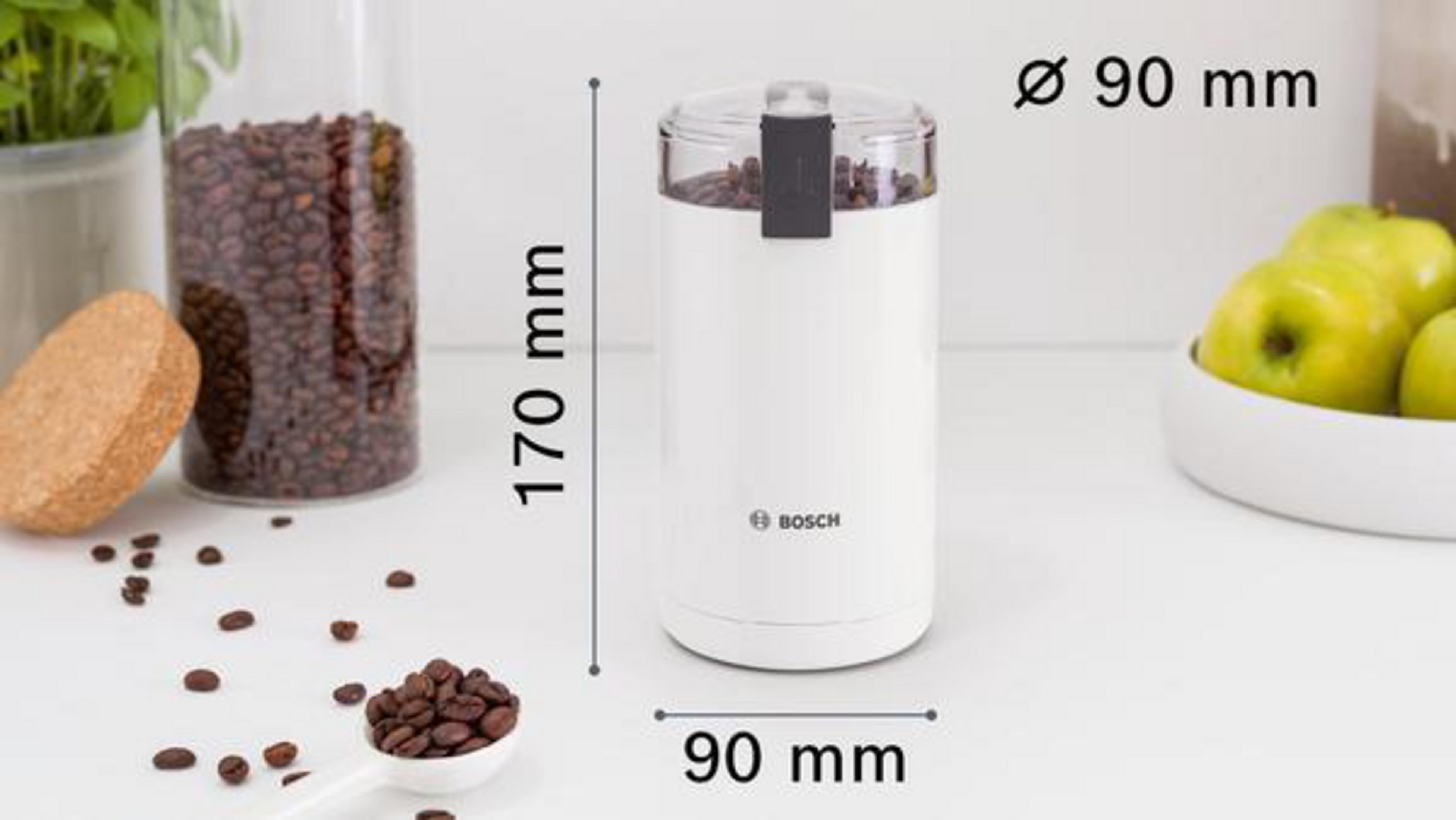 A white coffee grinder with dimensions, a scoop of beans, and a jar of beans in the background.