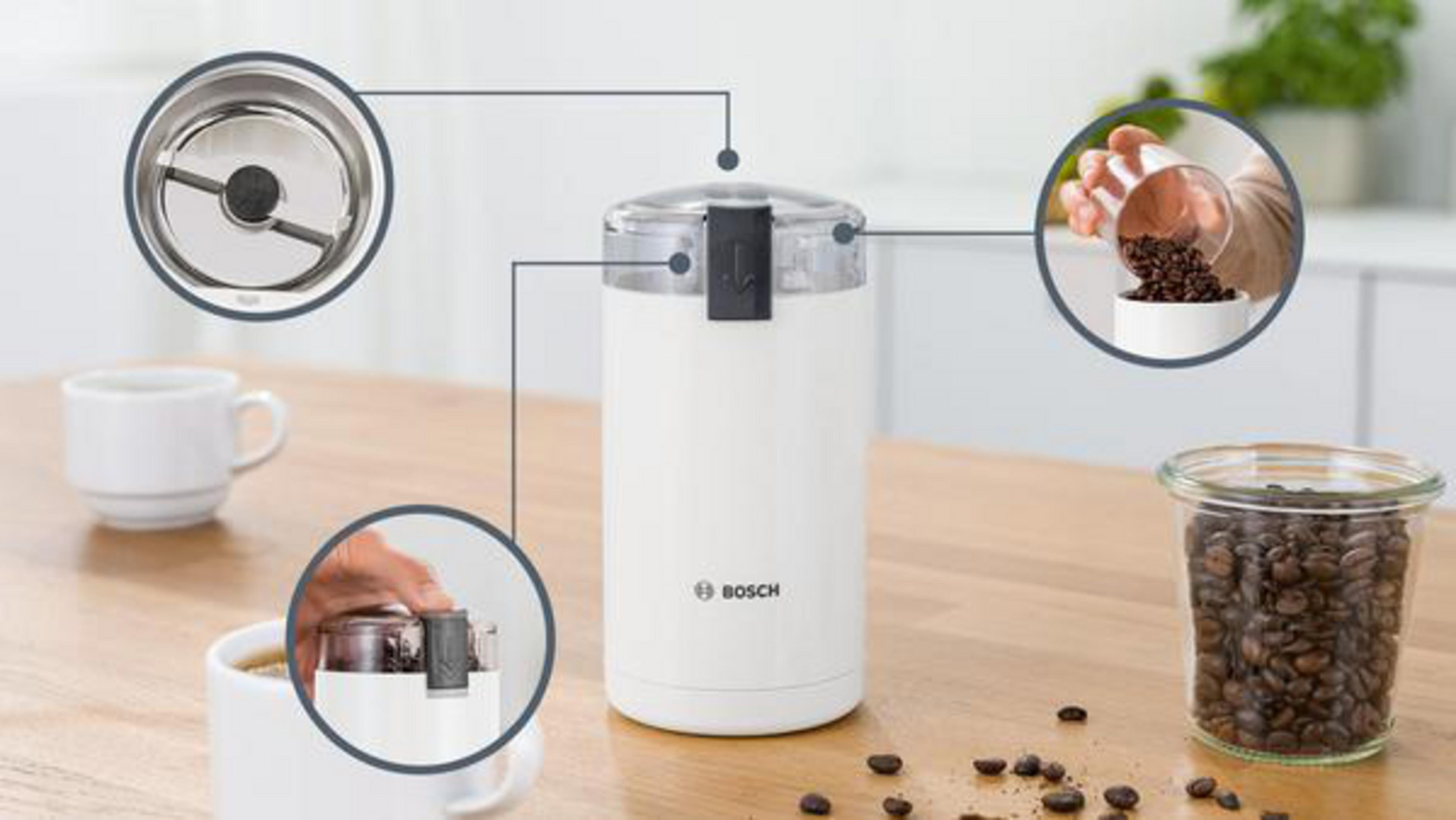 White coffee grinder with beans, a cup, and detailed internal components on a table.