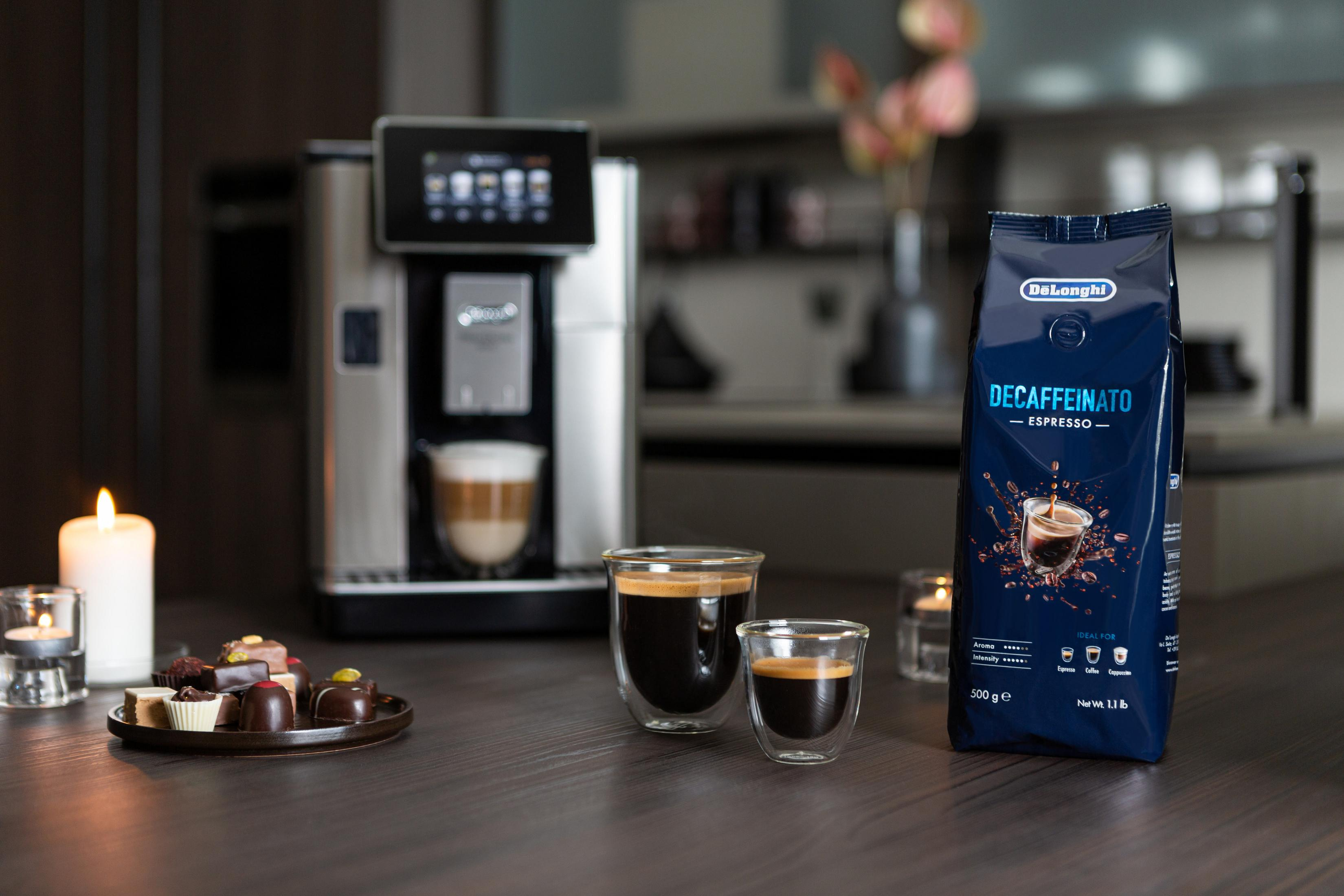 Kaffeemaschine, Kaffee und entkoffeinierter Kaffeebeutel. Kerzen und Gebäck auf einem Holztisch.