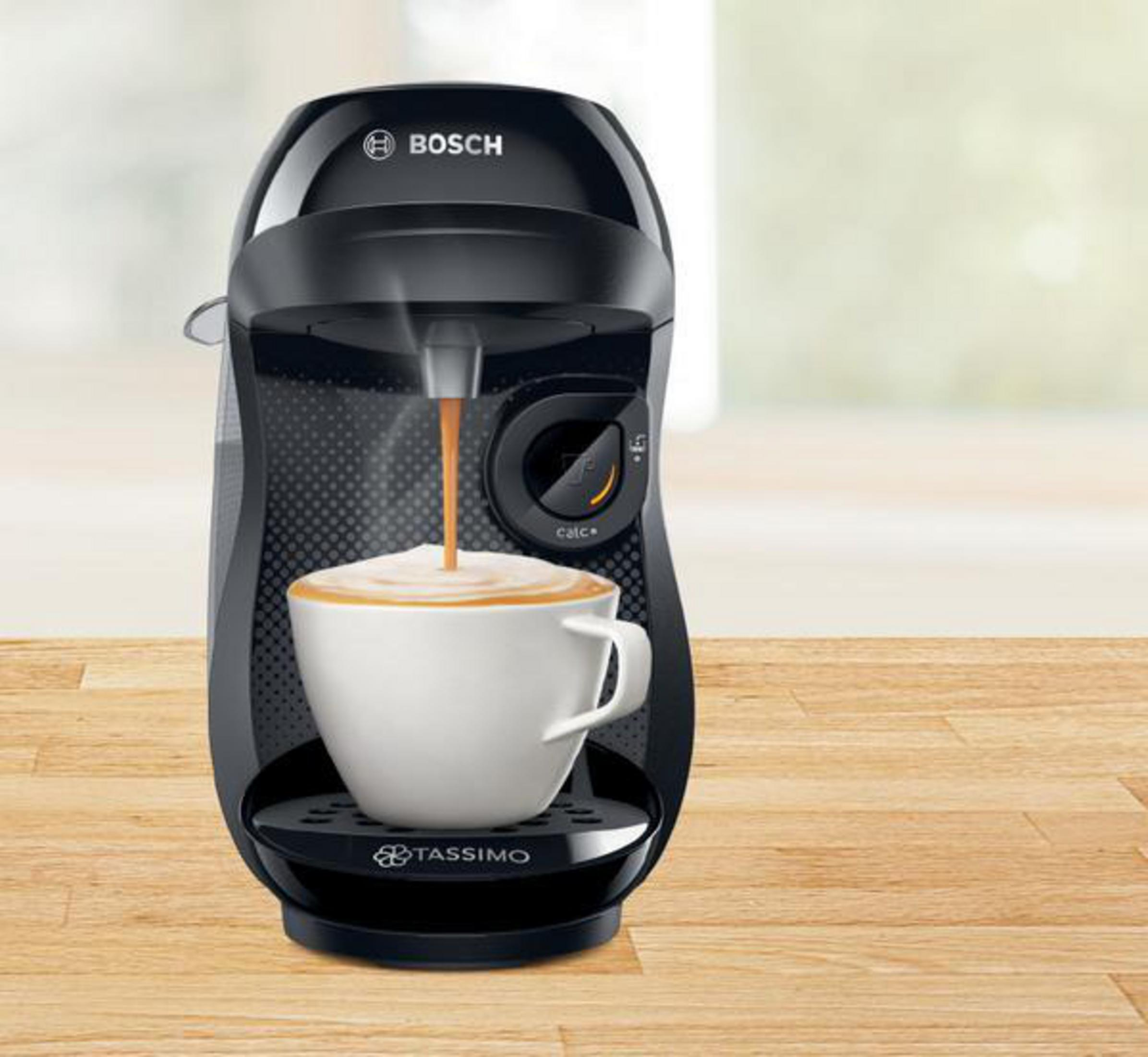Una macchina da caffè Tassimo nera e argento. Una tazza è sotto il beccuccio mentre il caffè viene versato.