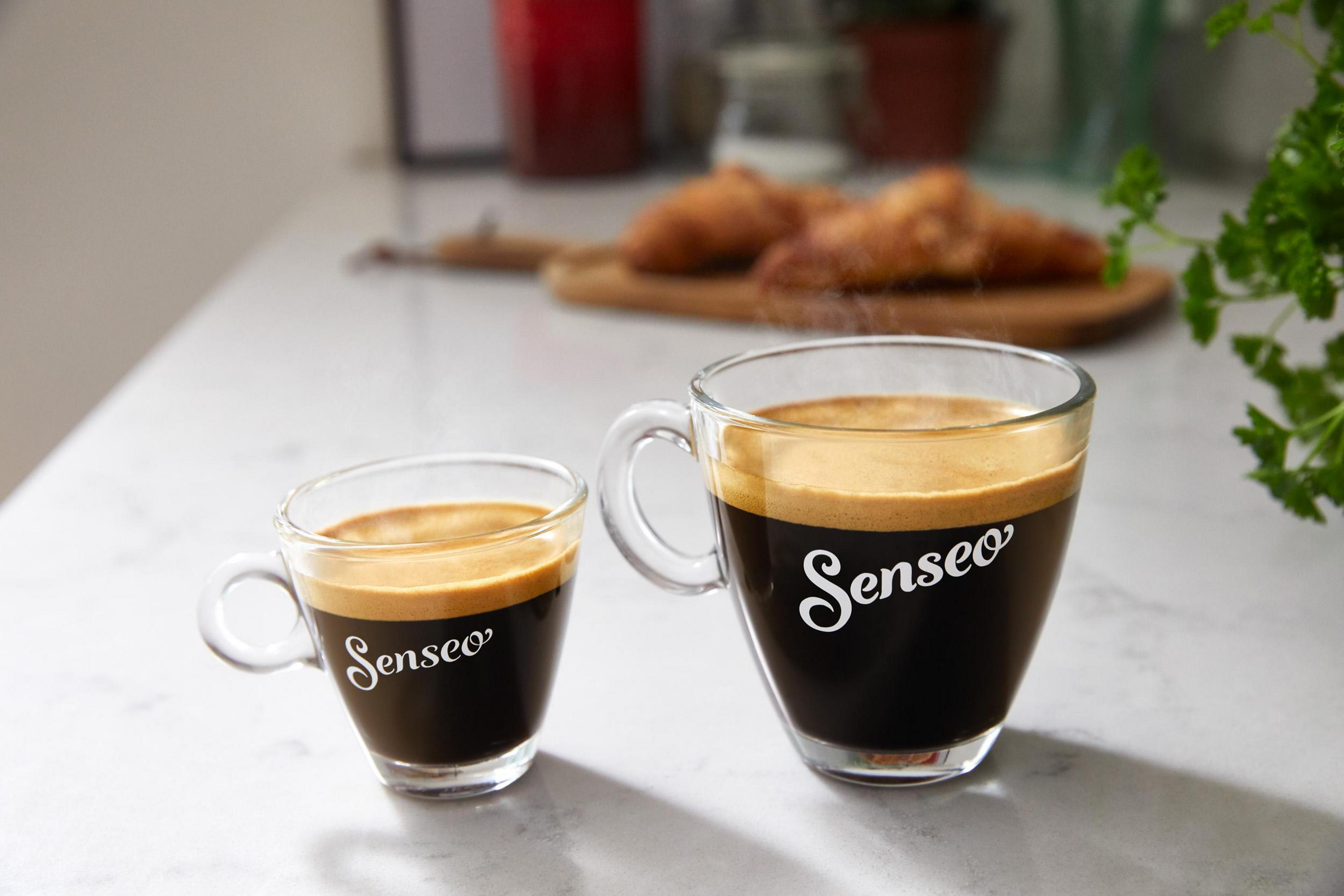 Due tazze di caffè con 'Senseo' e un pasticcino su un tagliere di legno.