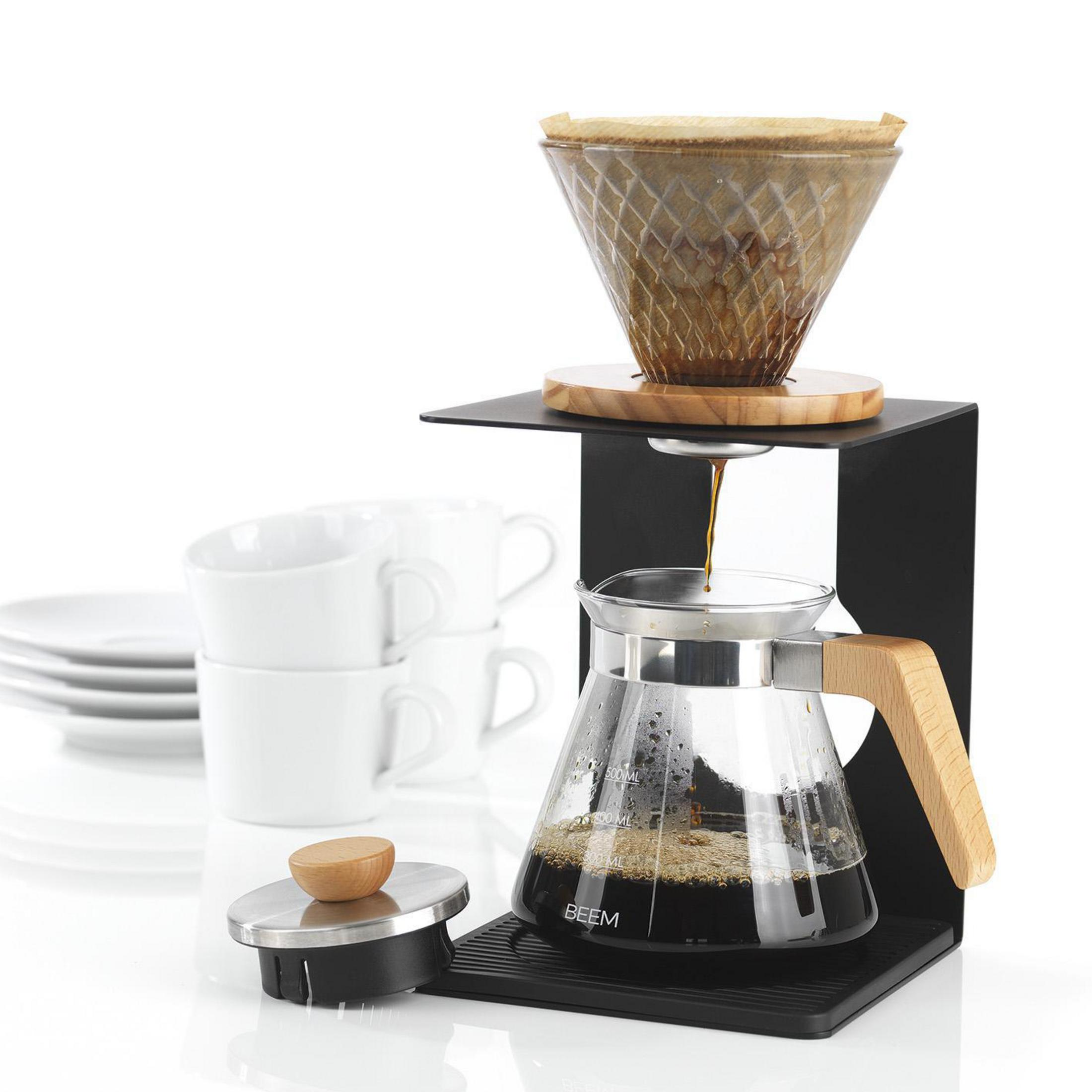 Eine Hand drückt einen Knopf an einer schwarzen Kaffeemaschine mit dem Text 'Automatische Dosierung' und 'Auto Stop'.