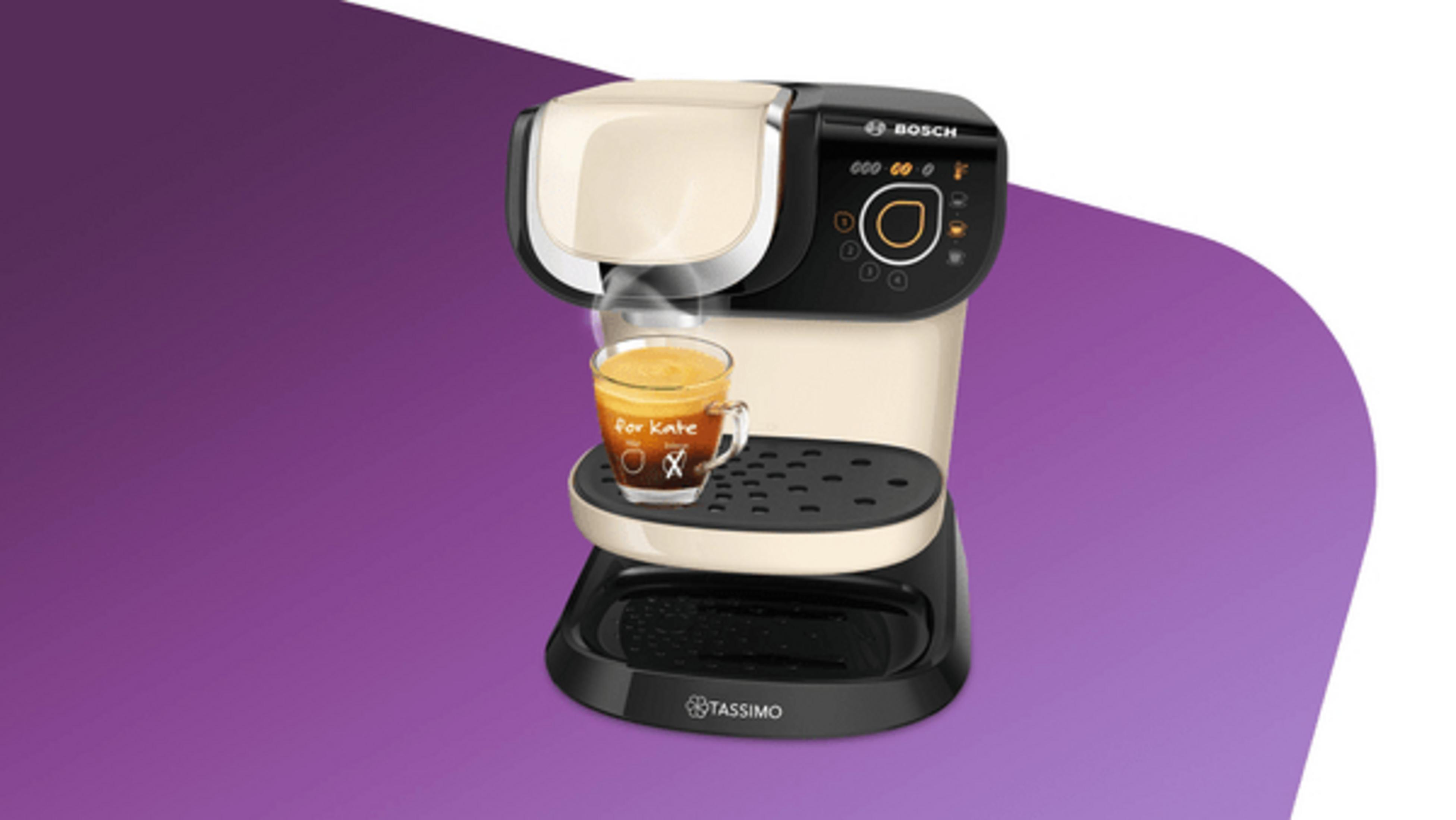 Cremefarbene und schwarze Tassimo Kaffeemaschine mit einem Glas Kaffee.