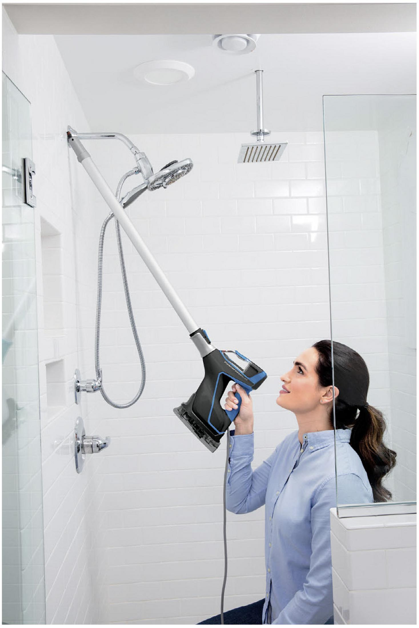 Kobieta czyści prysznic za pomocą długiego uchwytu w białej łazience.