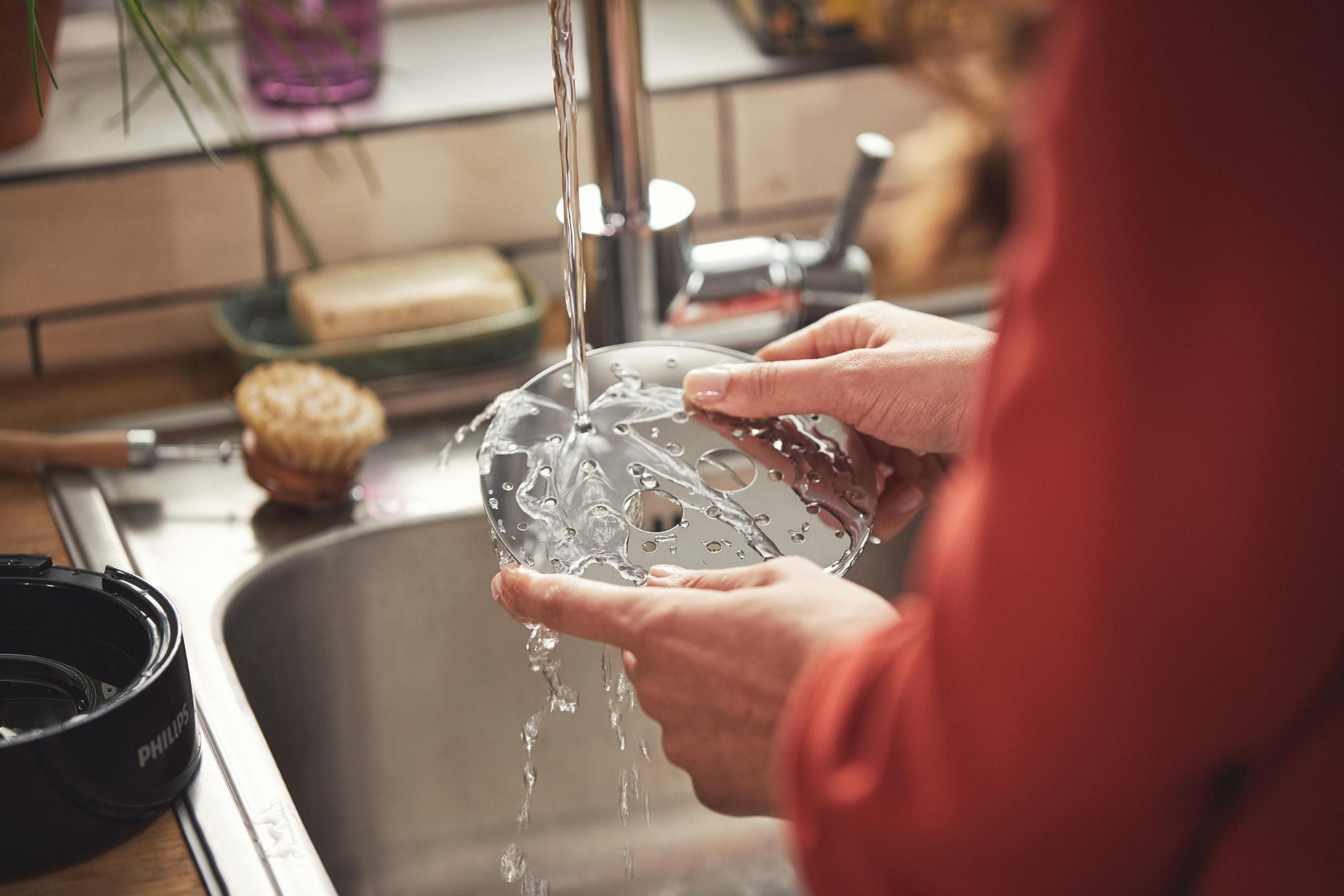 Ręce myjące część urządzenia kuchennego pod bieżącą wodą w zlewie. Widoczna czerwona koszula.